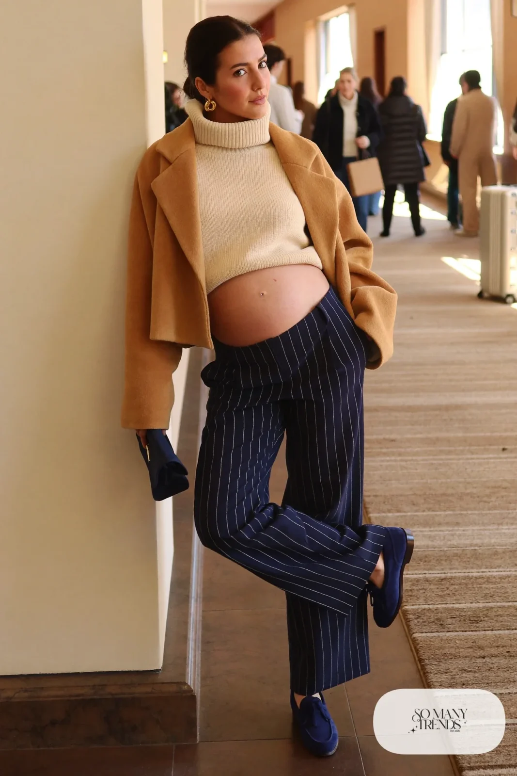 pregnant woman in navy pinstripe wide leg trousers, cream oversized turtleneck, cropped camel coat above bump, navy suede loafers, gold hoop earrings, navy clutch, outfit 18