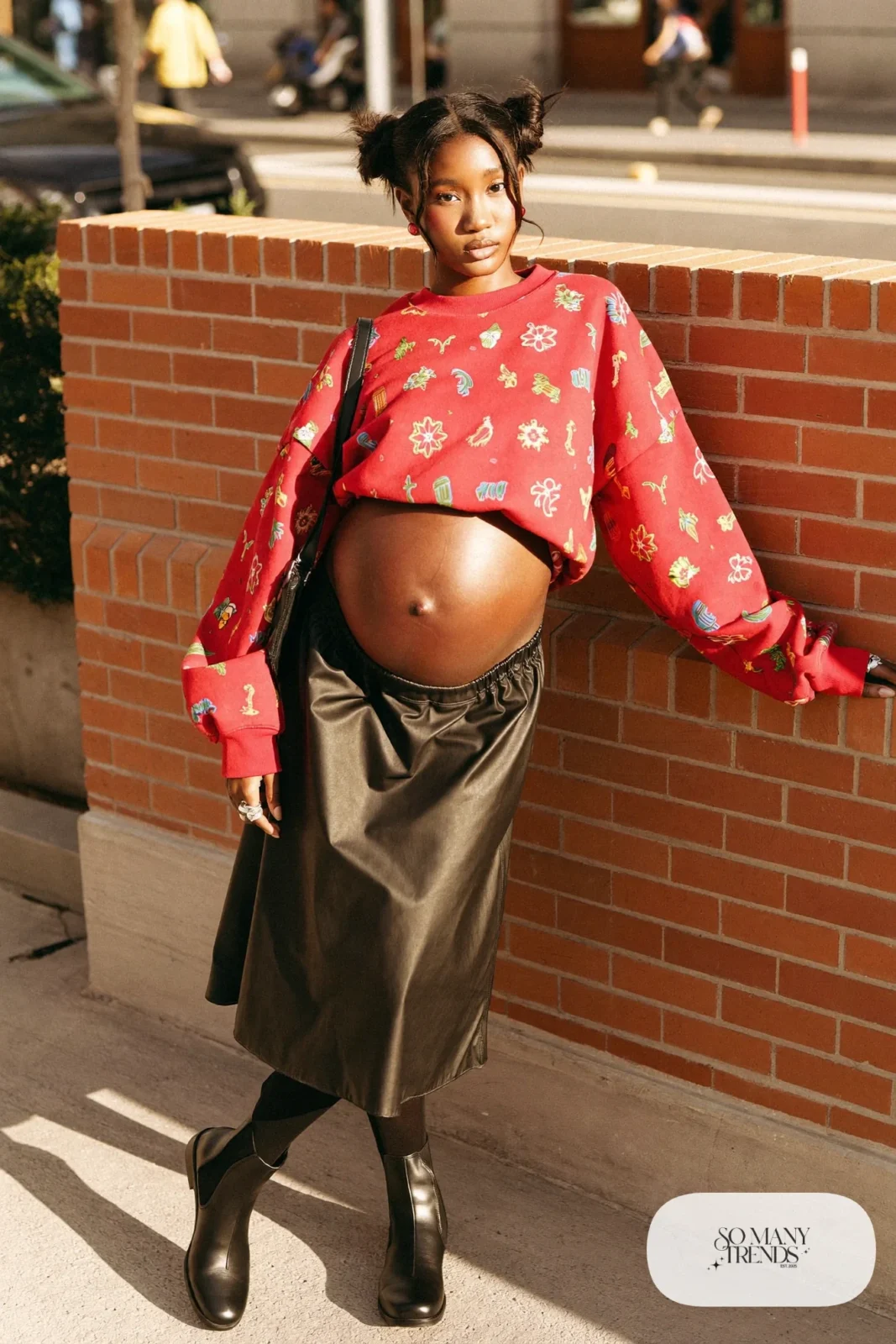 pregnant woman in red graphic boxy sweatshirt, black faux leather A-line midi skirt, black opaque tights, black Chelsea boots, small black crossbody, red stud earrings, outfit 25