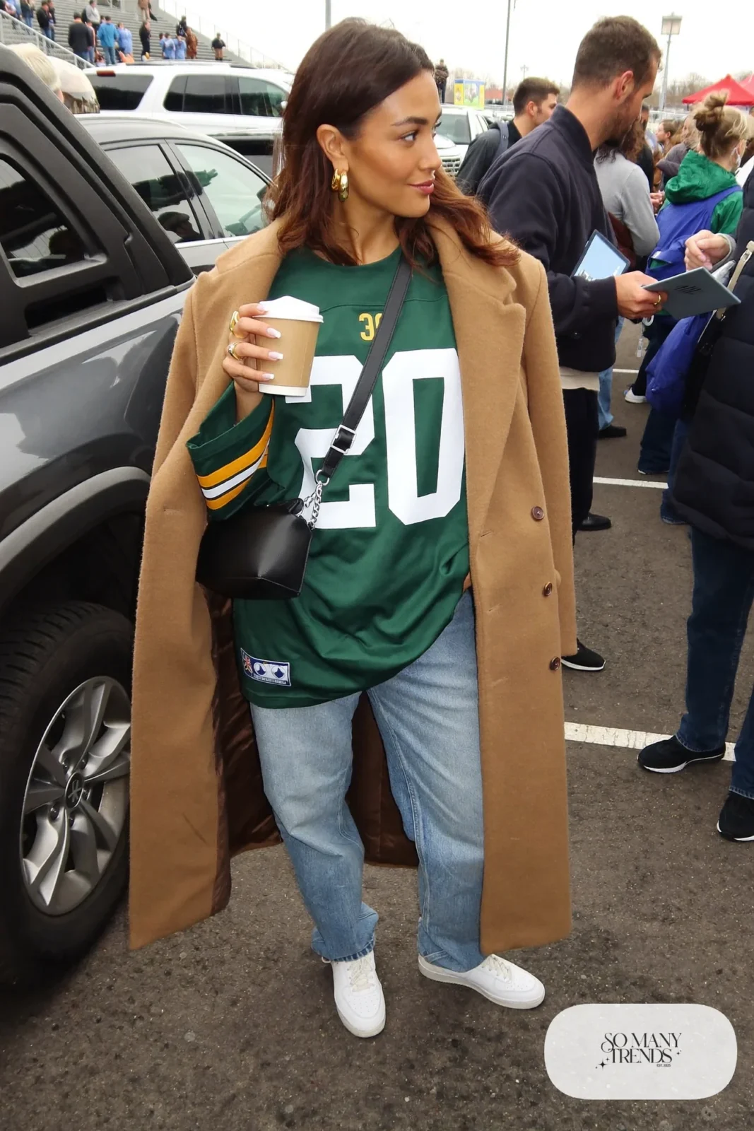 oversized forest green football jersey light wash straight jeans camel wool coat white sneakers crossbody bag outfit 1