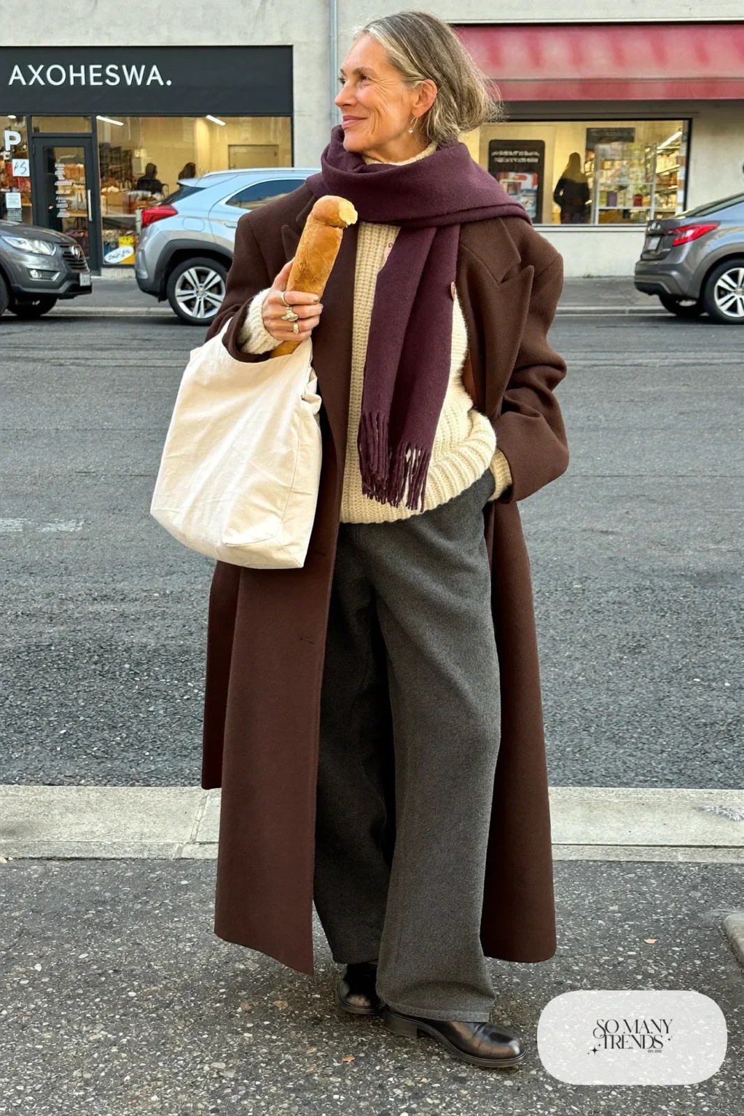 woman over 60 in long chocolate brown wool coat cream turtleneck gray wide-leg pants black ankle boots burgundy scarf outfit 1
