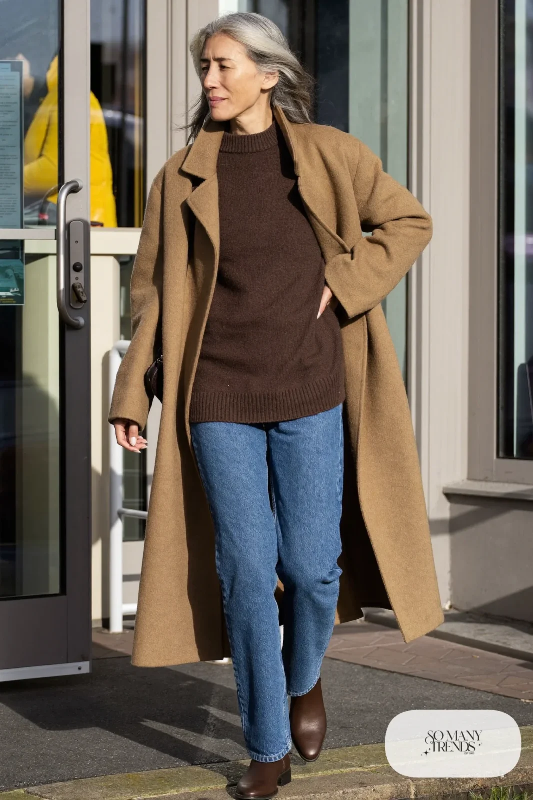 woman over 60 in camel wool coat brown sweater blue straight jeans brown ankle boots crossbody bag outfit 4