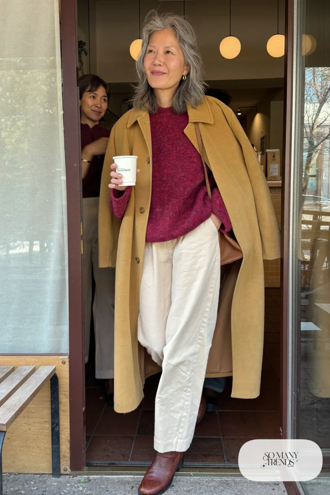 woman over 60 in wine red sweater cream wide-leg pants camel coat gold hoops brown ankle boots outfit 13