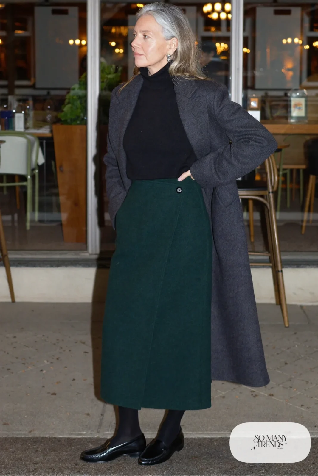 woman over 60 in dark green wool wrap skirt black turtleneck opaque tights long gray coat loafers outfit 28