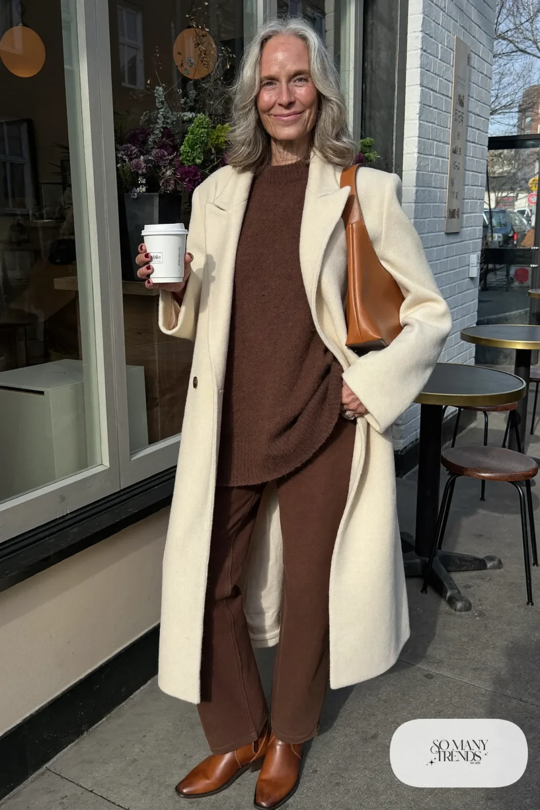 woman over 60 in cream wool coat chocolate brown sweater brown straight pants brown boots camel bag outfit 31