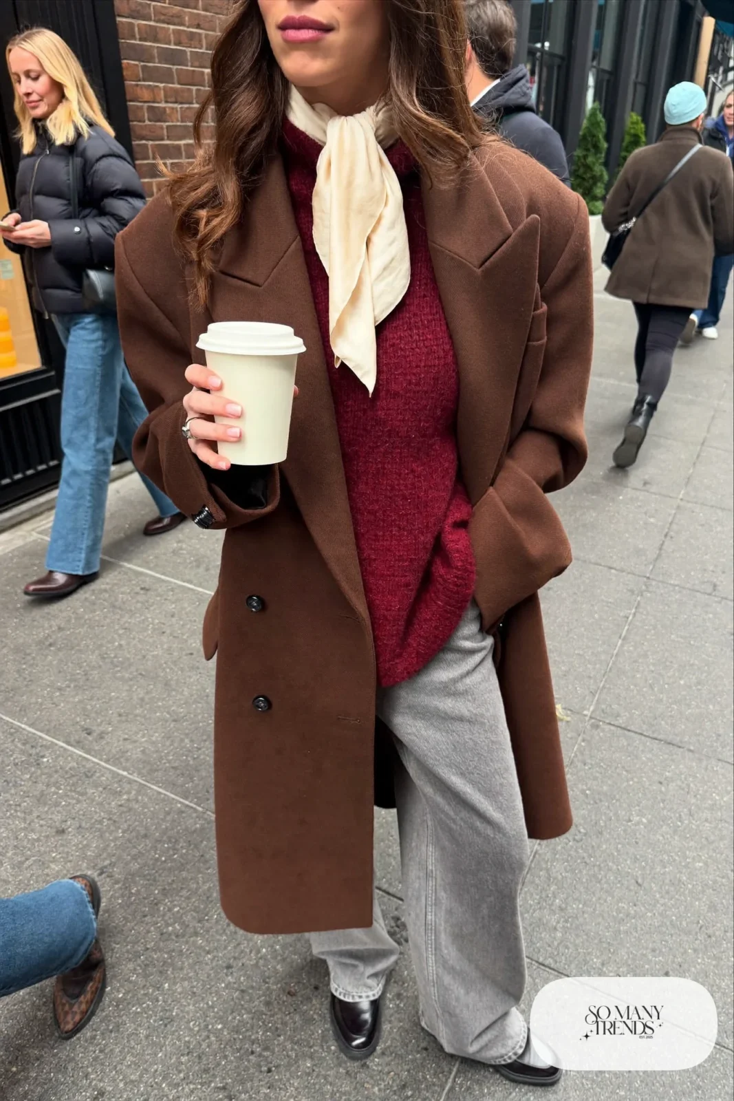 Long chocolate brown wool coat, burgundy chunky sweater, gray wide-leg jeans, cream scarf, black loafers with socks, winter outfit 1
