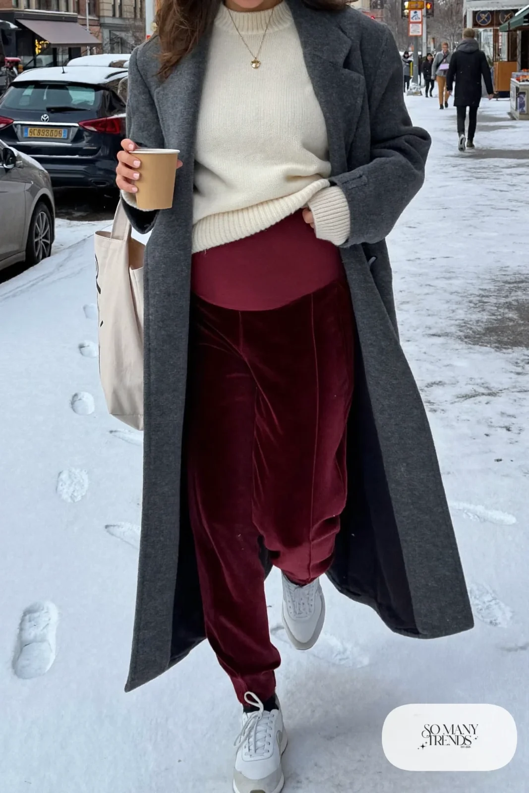 pregnant woman in burgundy velvet maternity joggers, cream chunky knit sweater, white sneakers and long coat, outfit 18