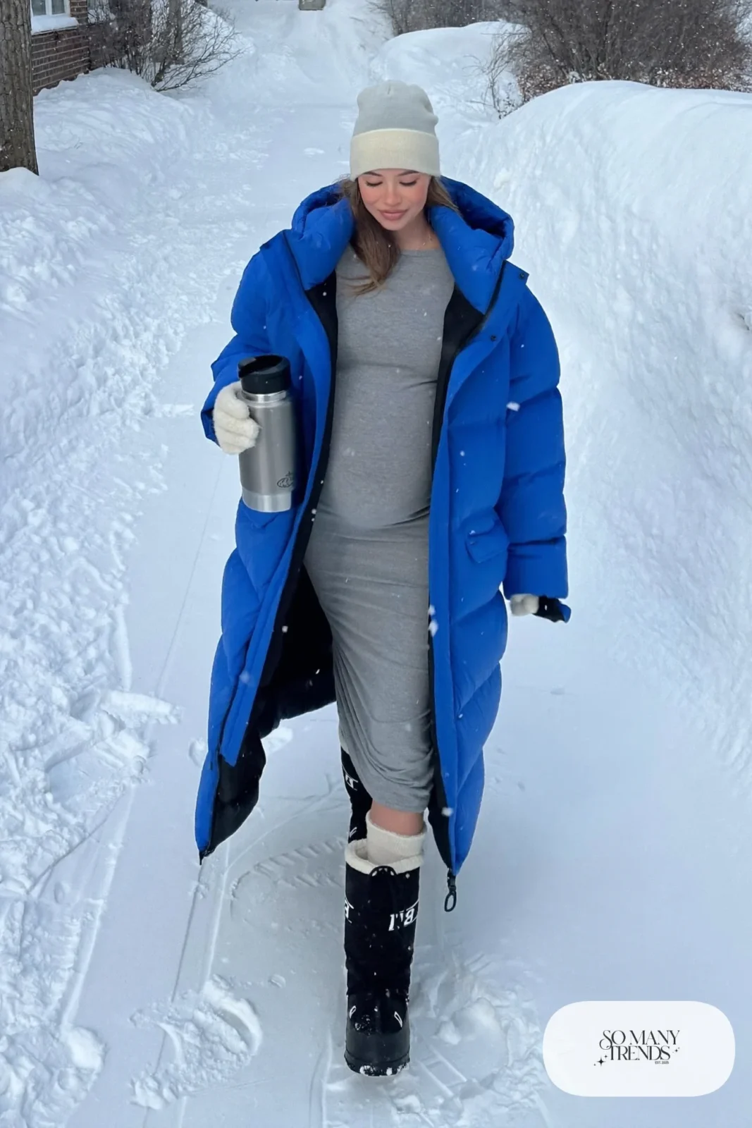 pregnant woman in cobalt blue long puffer jacket, gray knit dress, waterproof snow boots and wool hat, outfit 28