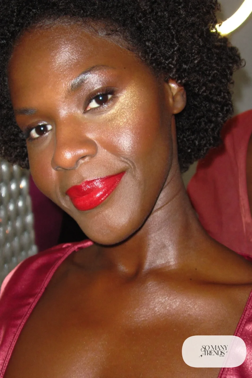 woman with deep skin wearing bold red lipstick and gold highlighter on cheekbones, makeup look 3