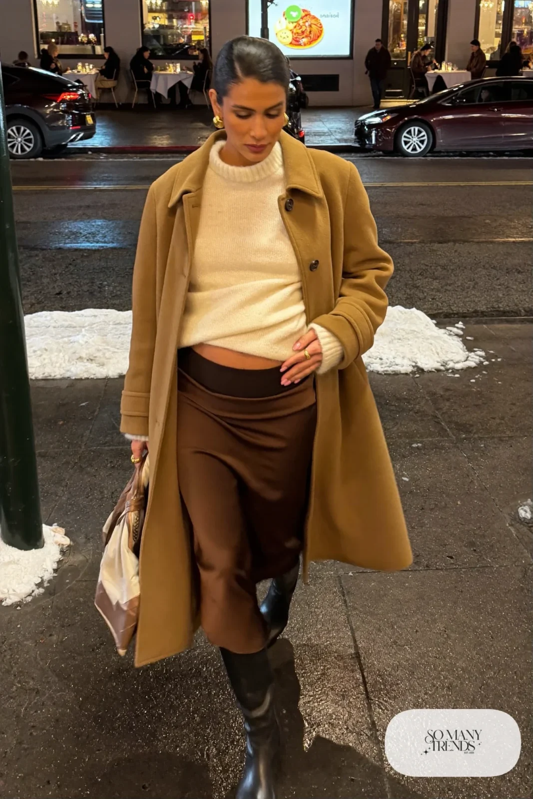 pregnant woman in chocolate satin midi skirt, cream knit sweater, black knee-high boots and camel coat, outfit 24