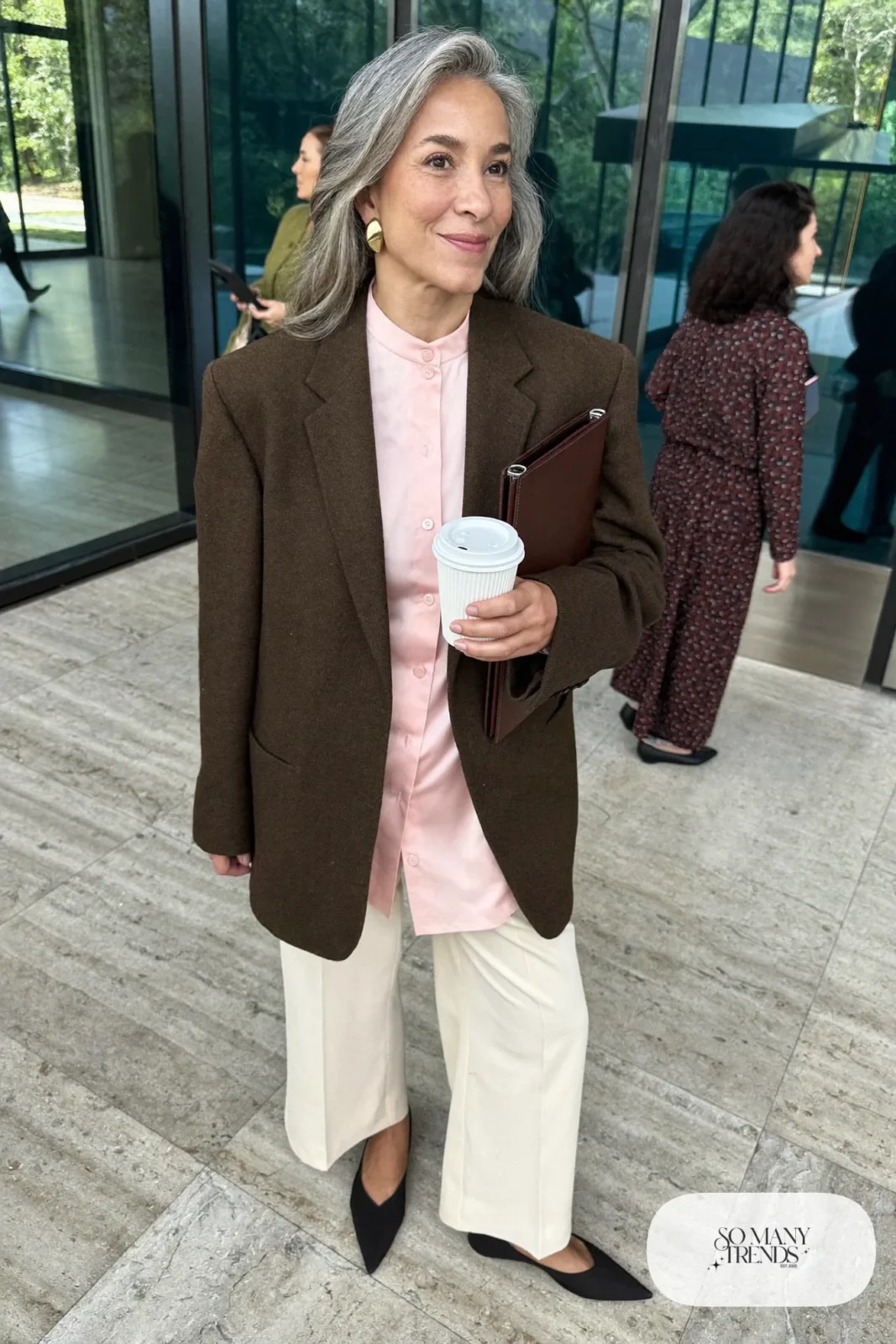 Woman in her fifties in a long espresso brown blazer, pale pink blouse, ivory wide-leg pants and pointed-toe flats, outfit 1