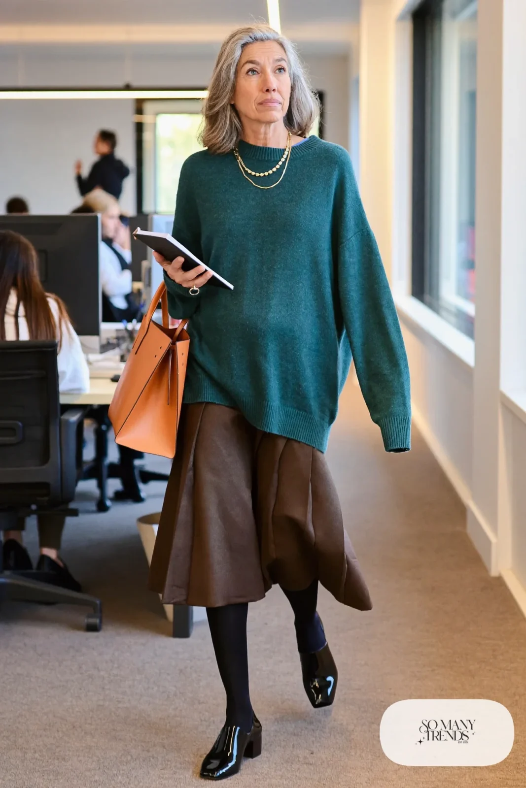 Woman in her fifties in a teal knit sweater, espresso pleated midi skirt, sheer black tights and black loafers, outfit 2