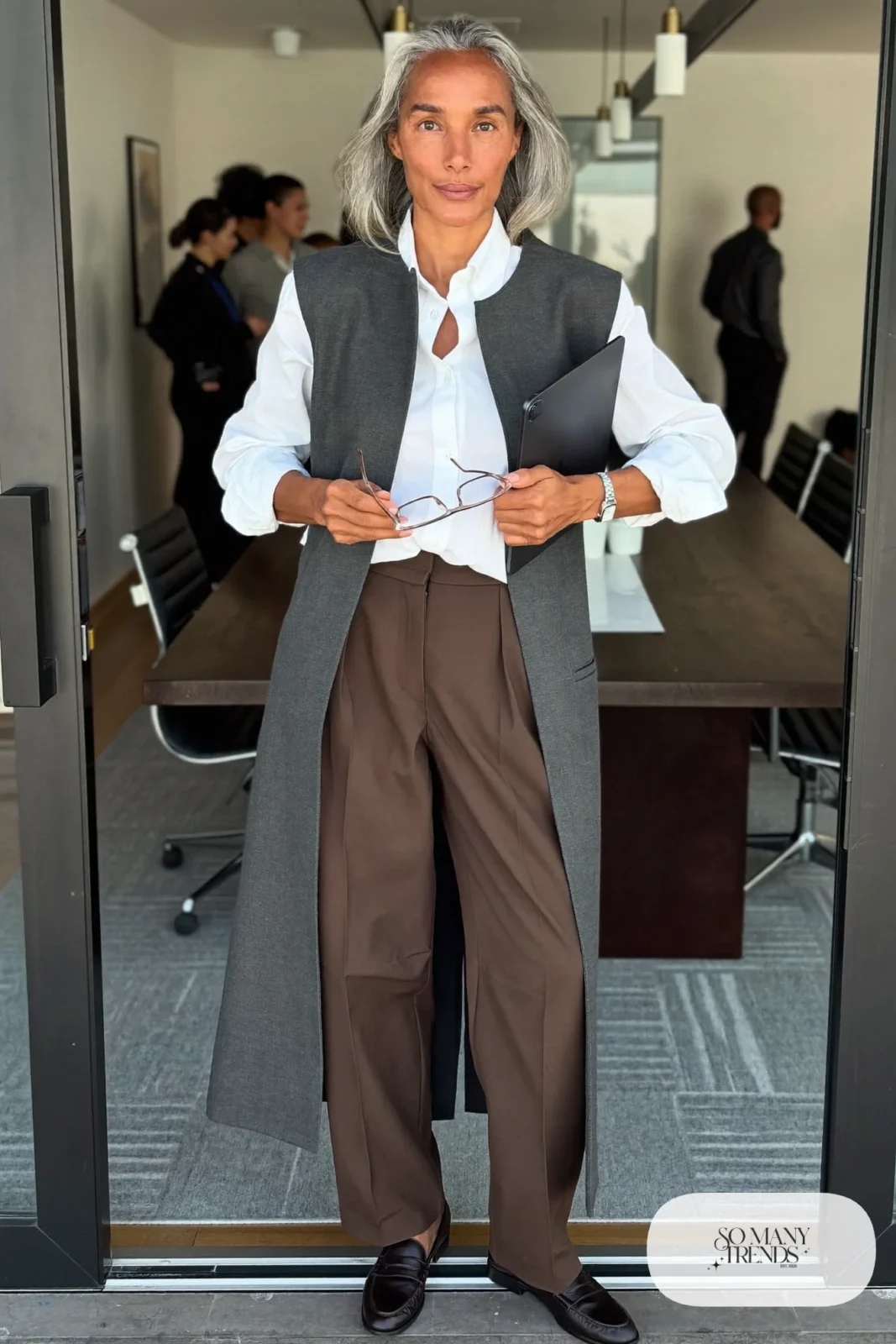 Woman in her fifties in a long charcoal tailored vest, white shirt, straight espresso pants and loafers, outfit 3