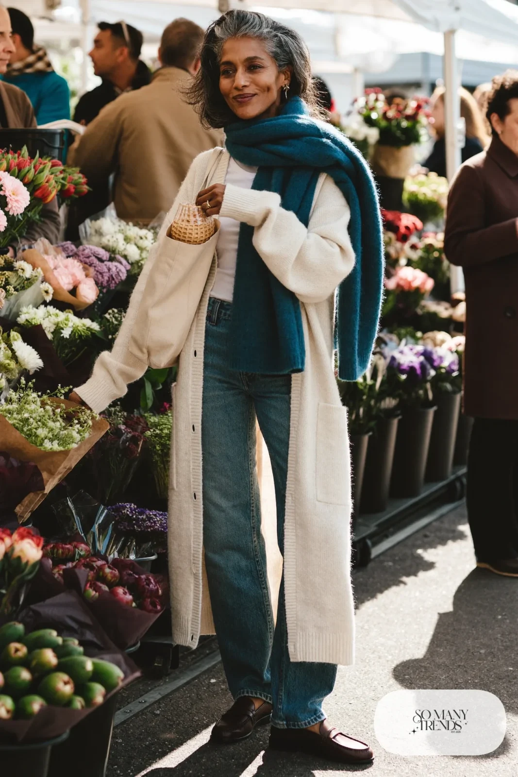Woman in her fifties in straight mid-wash jeans, long cream cardigan, teal scarf and brown loafers, outfit 8