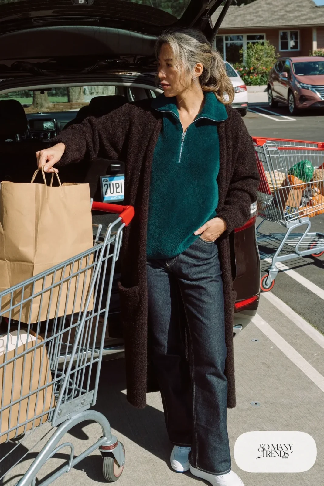Woman in her fifties in a teal quarter-zip pullover, dark barrel-leg jeans and white leather sneakers, outfit 11