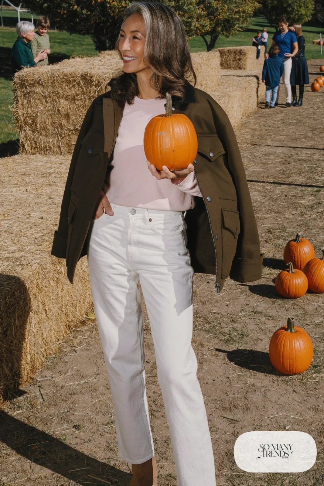 Woman in her fifties in white jeans, olive utility jacket, pink tee and tan ankle boots, outfit 14