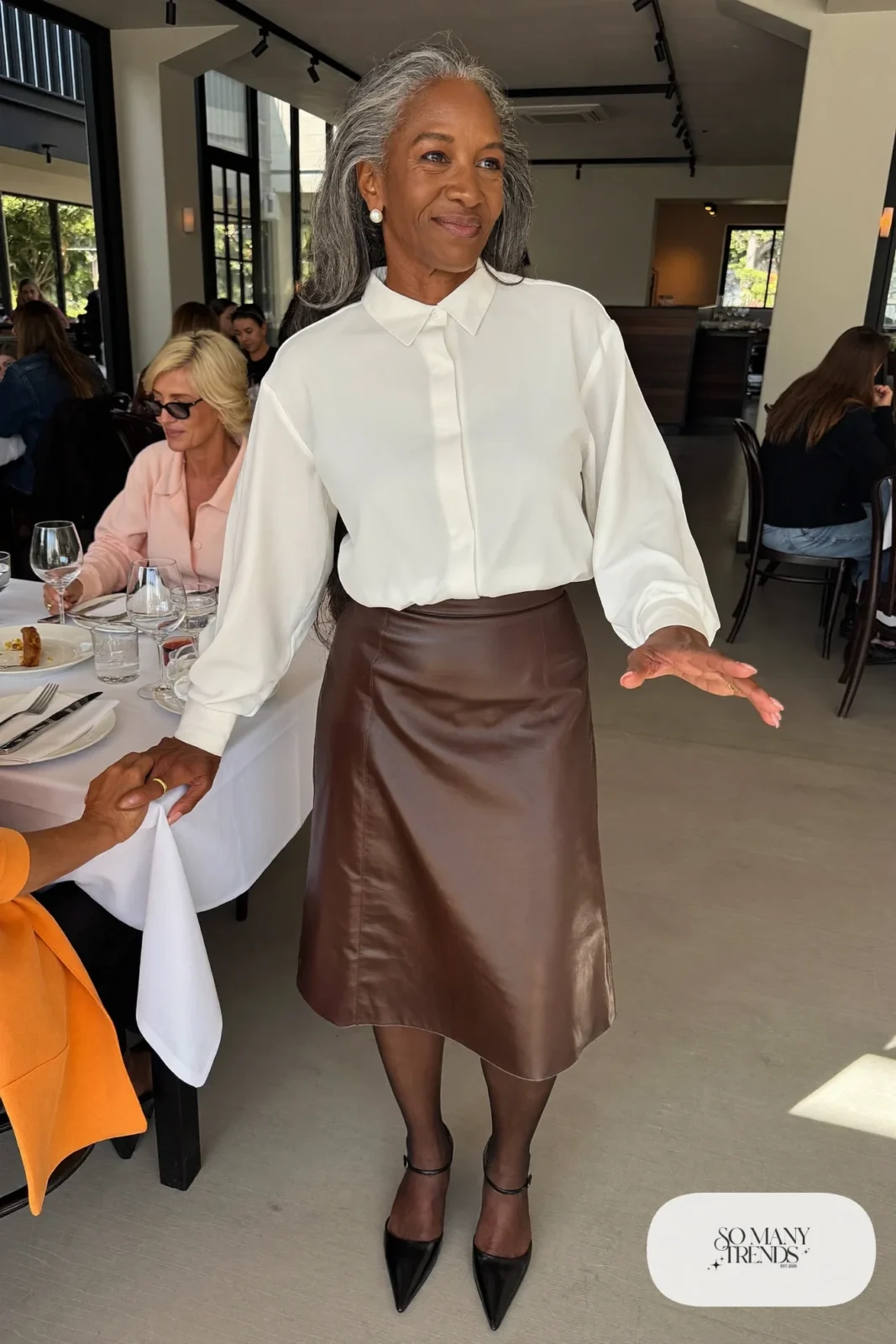 Woman in her fifties in an ivory blouse, espresso faux leather midi skirt, black tights and closed-toe slingbacks, outfit 15