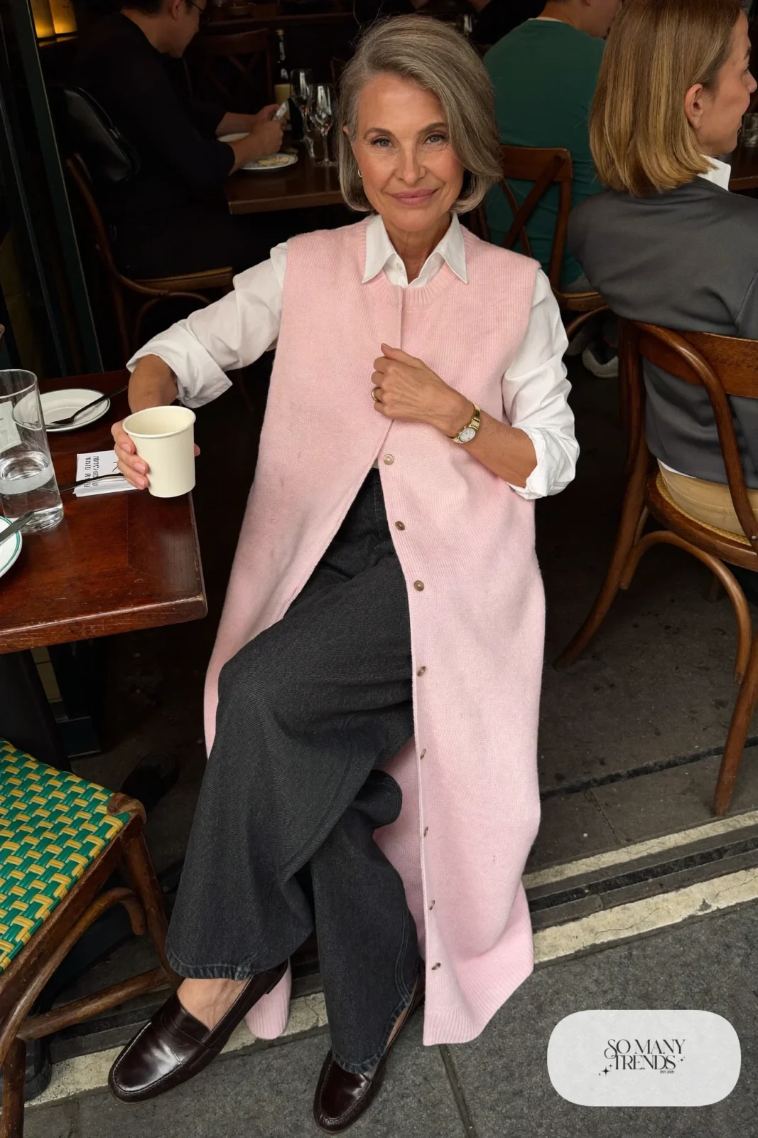 Woman in her fifties in a pale pink knit vest, white shirt, straight dark jeans and loafers, outfit 20