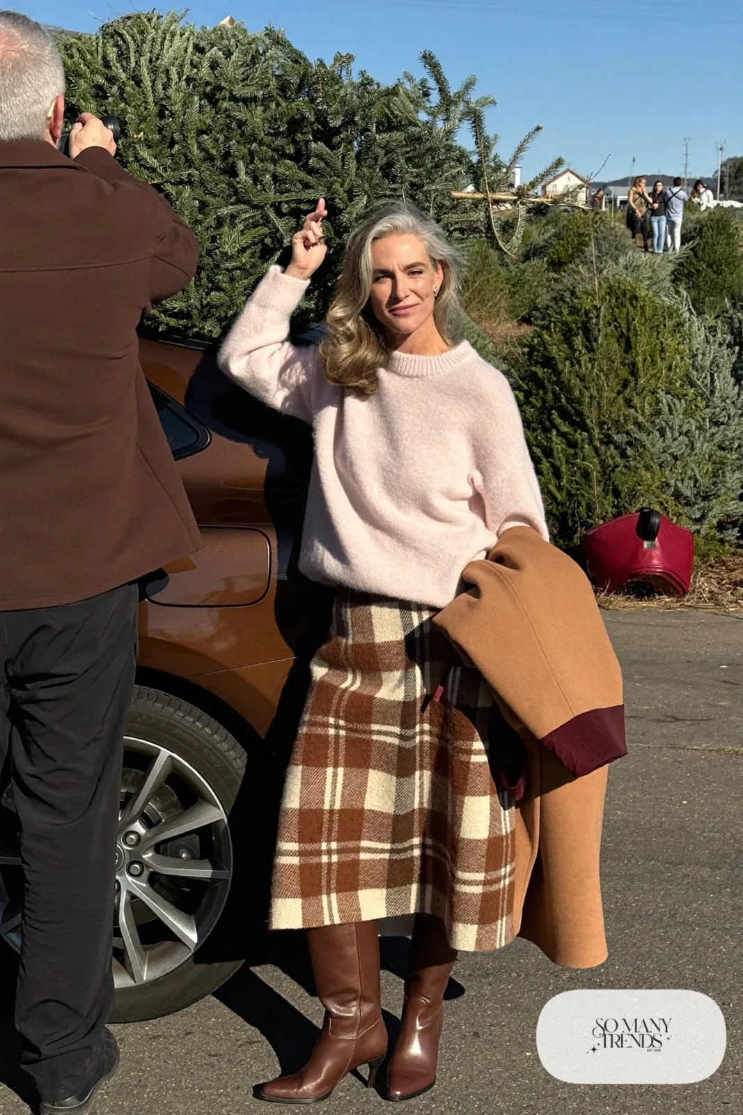 Woman in her fifties in a pale pink sweater, brown and cream plaid midi skirt, tights and tall brown boots, outfit 25