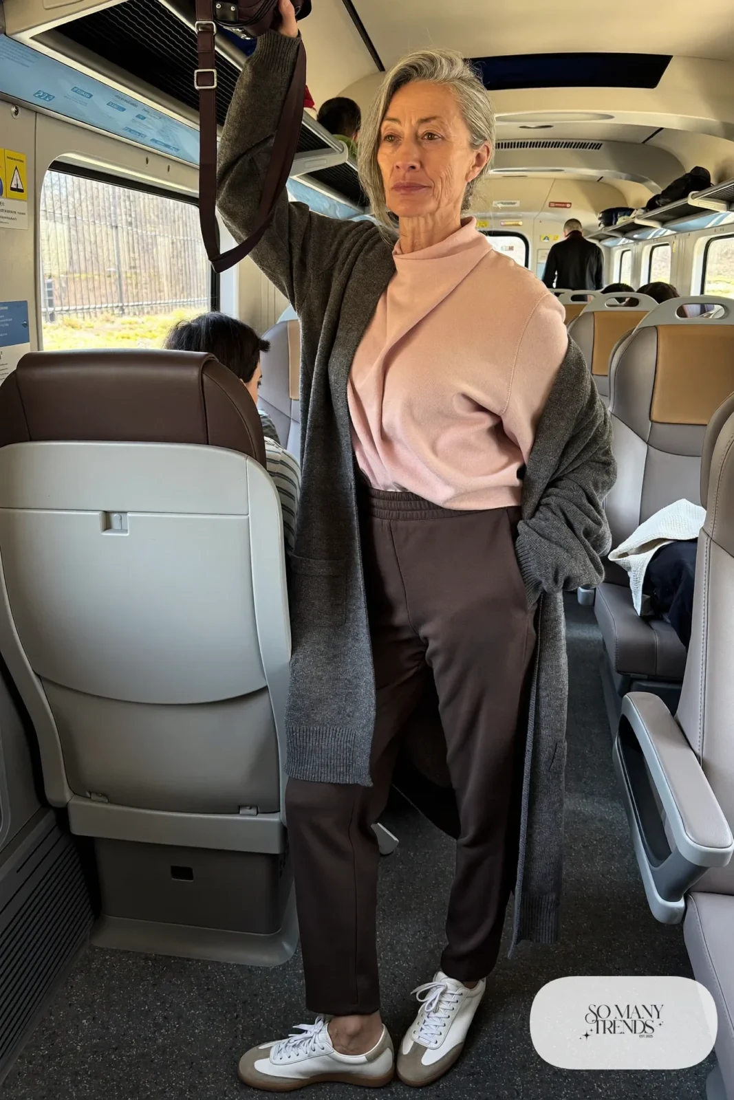 Woman in her fifties in espresso twill joggers, pale pink wrap sweater and leather sneakers on a train, outfit 30