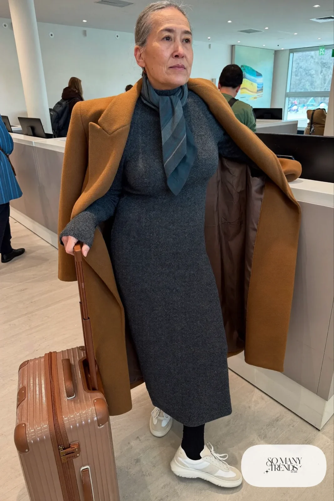 Woman in her fifties in a charcoal knit maxi dress, long camel coat, tights and cushioned sneakers, outfit 32