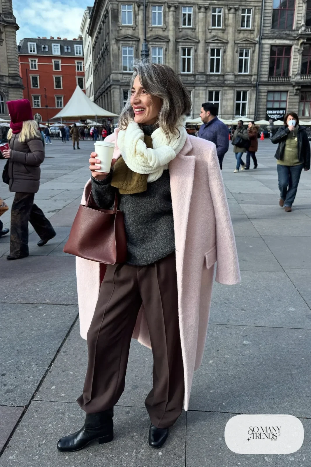 Woman in her fifties in a pale pink long wool coat, charcoal knit, straight pants and black boots, outfit 34