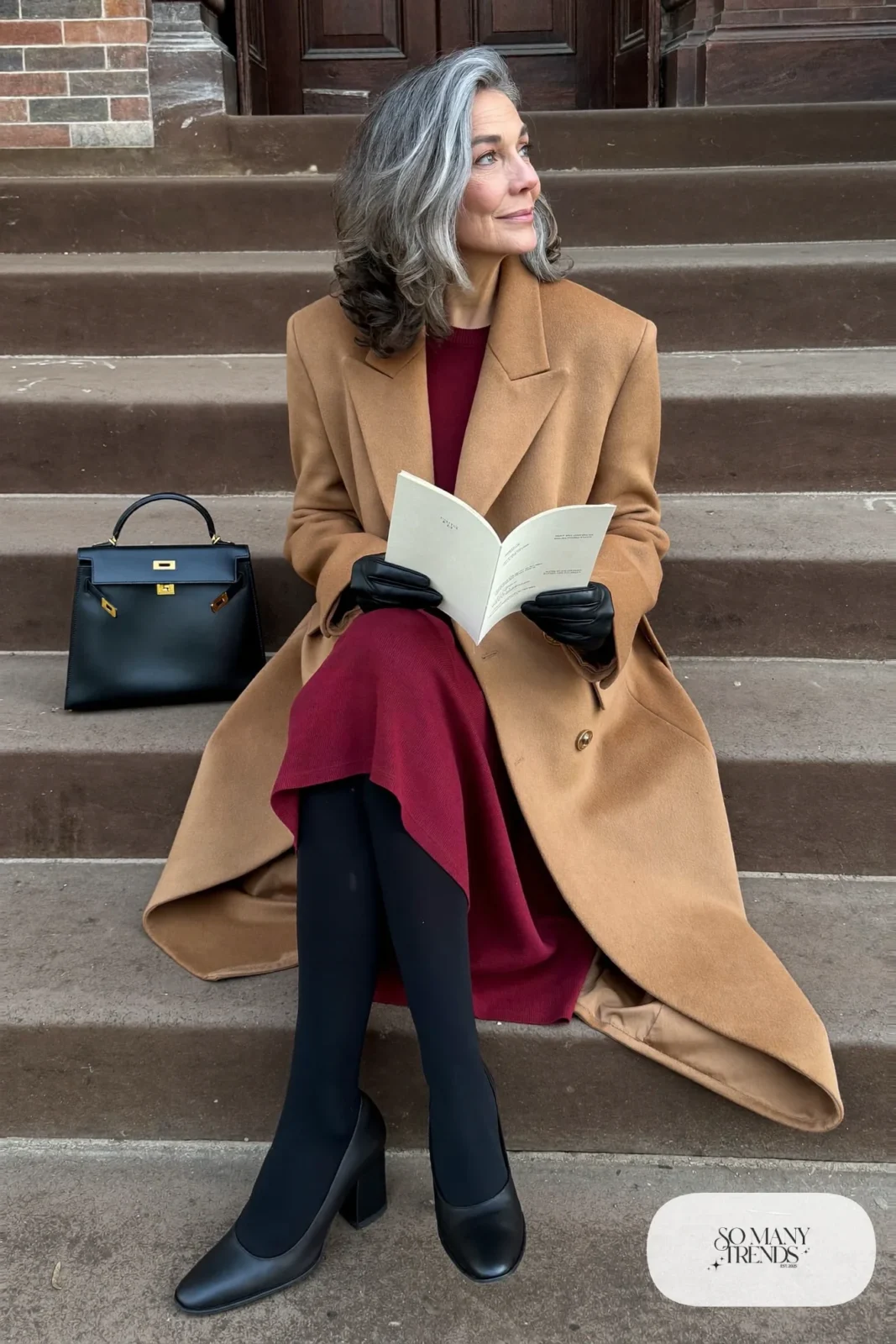 Woman in her sixties wearing a long camel coat open over a burgundy knit midi dress, sheer black tights and black block-heel pumps, outfit 2