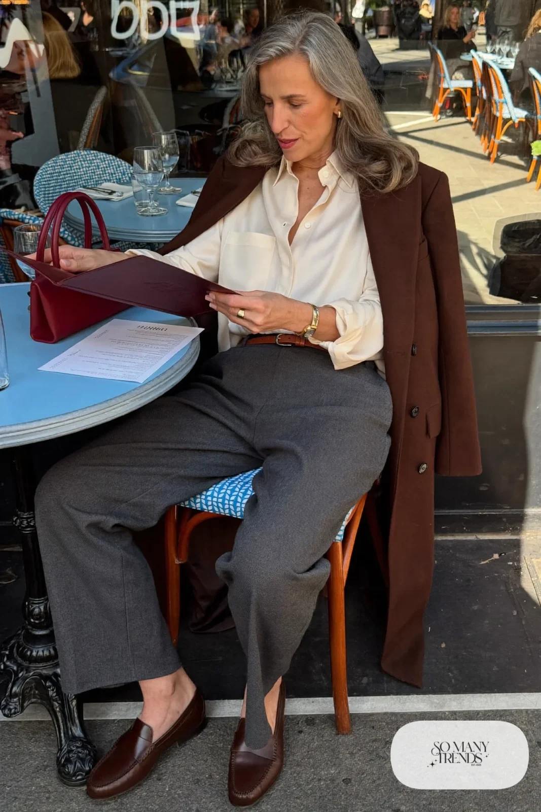 Woman in her sixties wearing charcoal straight-leg pants, a cream blouse tucked at the front, a brown belt and brown loafers, outfit 3