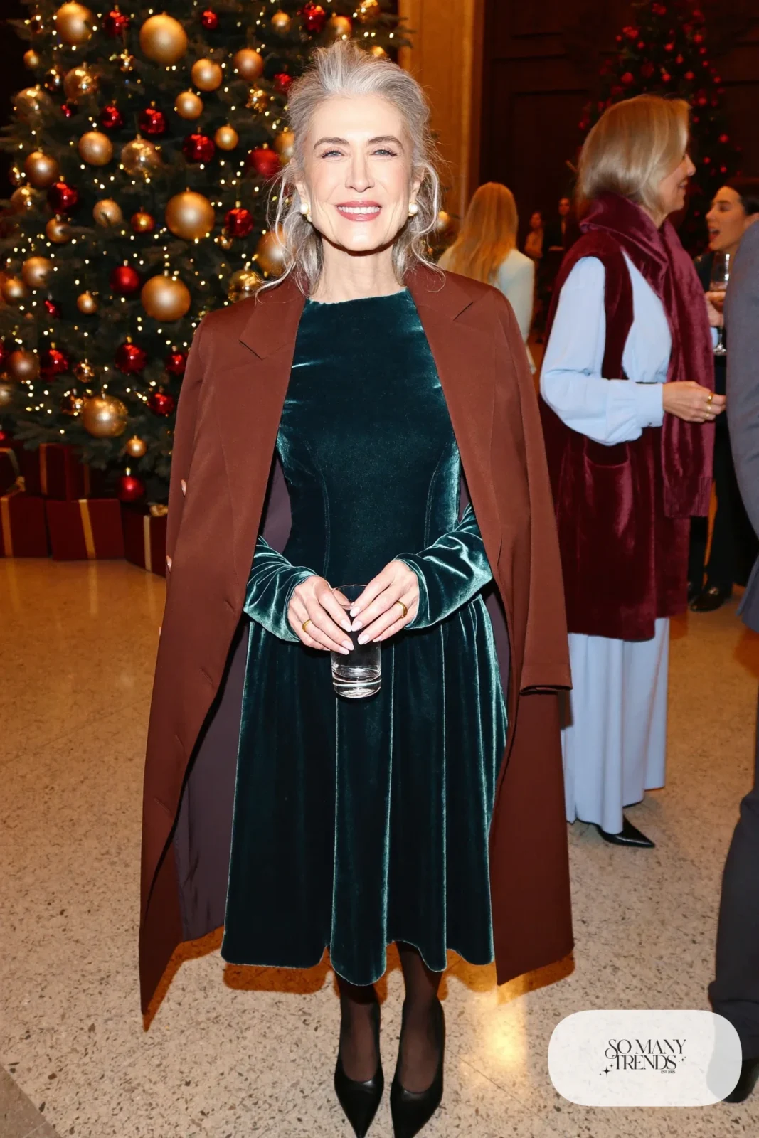Woman in her sixties wearing a forest green long-sleeve velvet midi dress, sheer black tights, black pointed pumps and pearl earrings, outfit 4