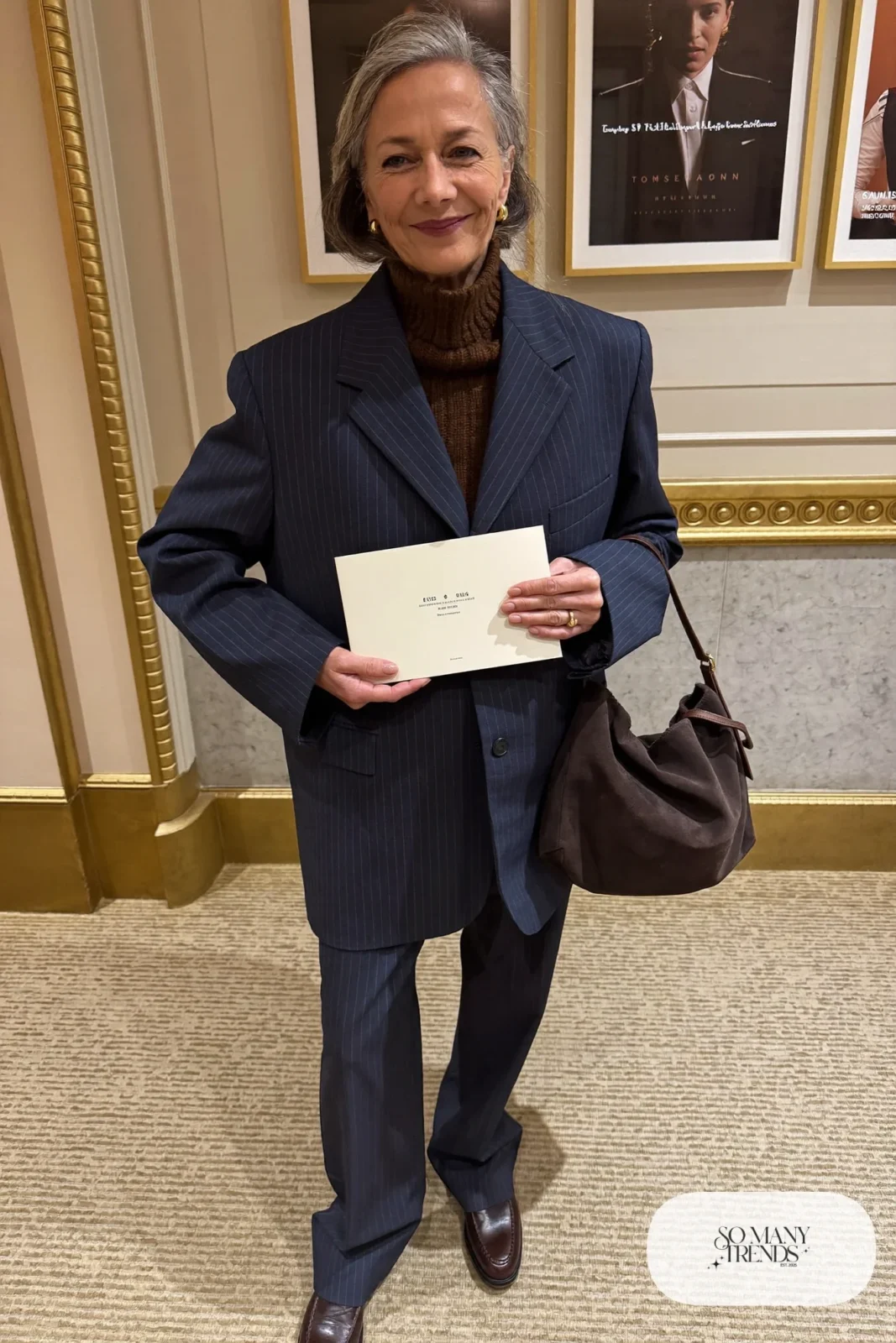 Woman in her sixties wearing an oversized navy pinstripe blazer, a brown ribbed turtleneck, navy straight pants and brown suede pouch bag, outfit 5