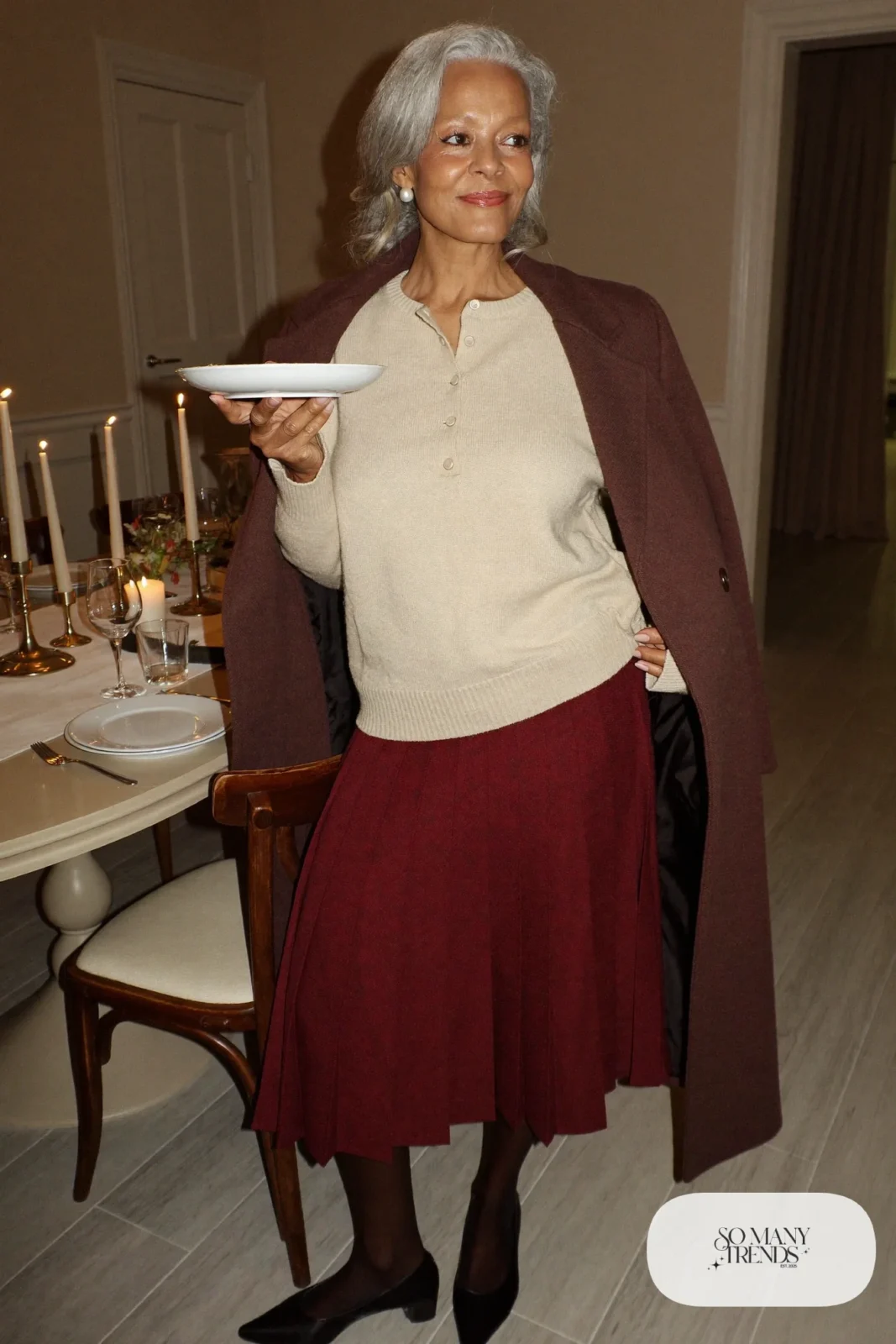 Woman in her sixties wearing a burgundy pleated midi skirt, a cream fine-knit sweater, sheer tights and black low-heel pumps, outfit 9