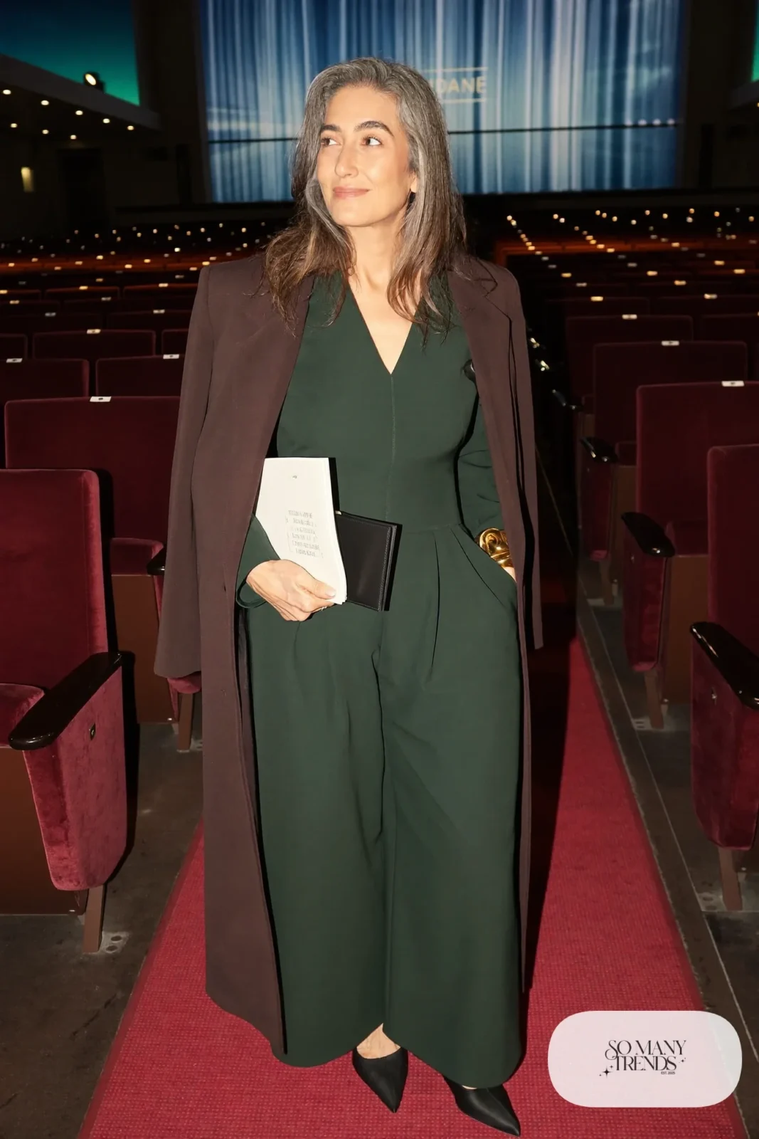 Woman in her sixties wearing a forest green wide-leg jumpsuit, black pointed flats and a gold cuff bracelet, outfit 11