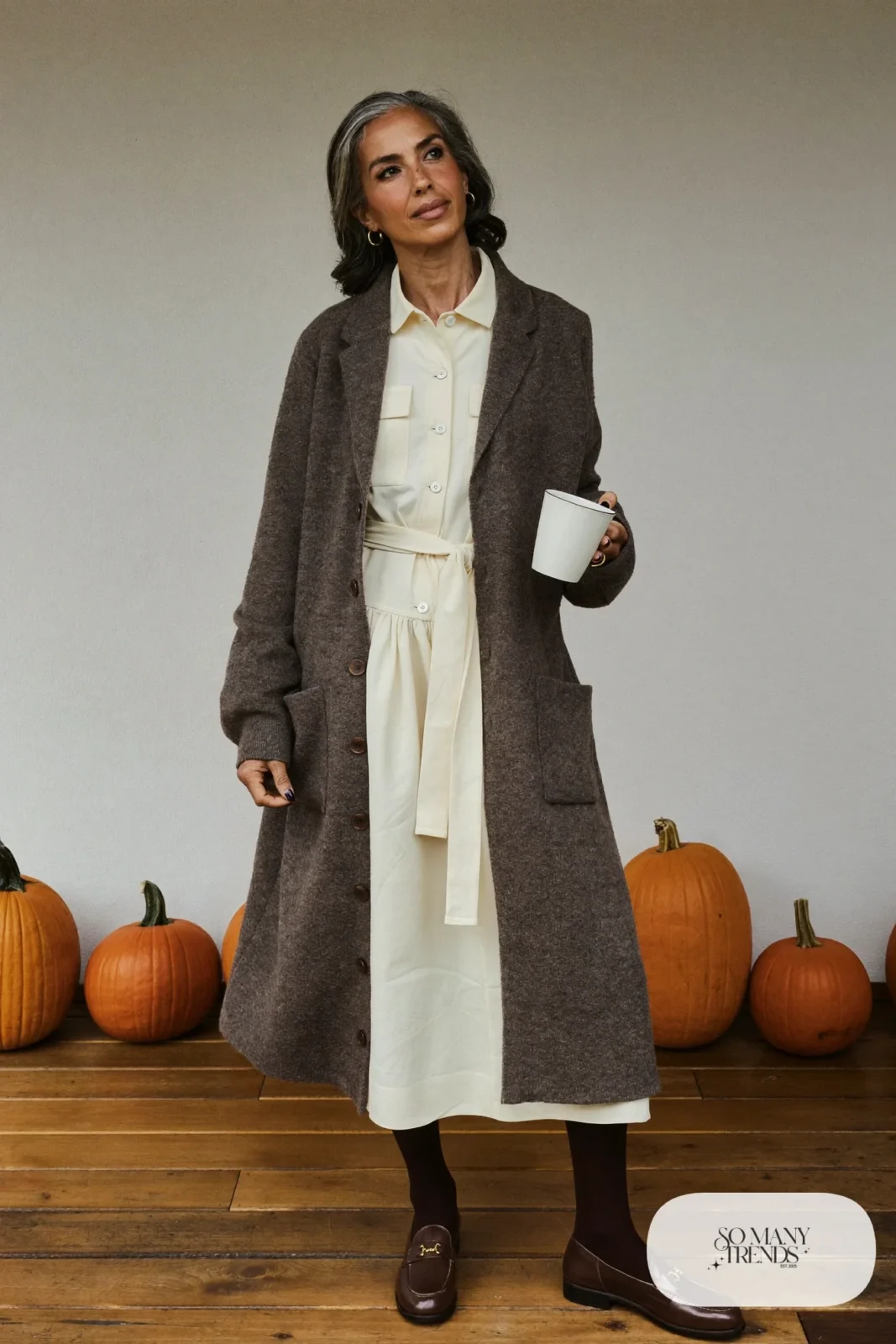Woman in her sixties wearing a cream shirtdress with a long gray cardigan coat, sheer tights and brown loafers, outfit 13