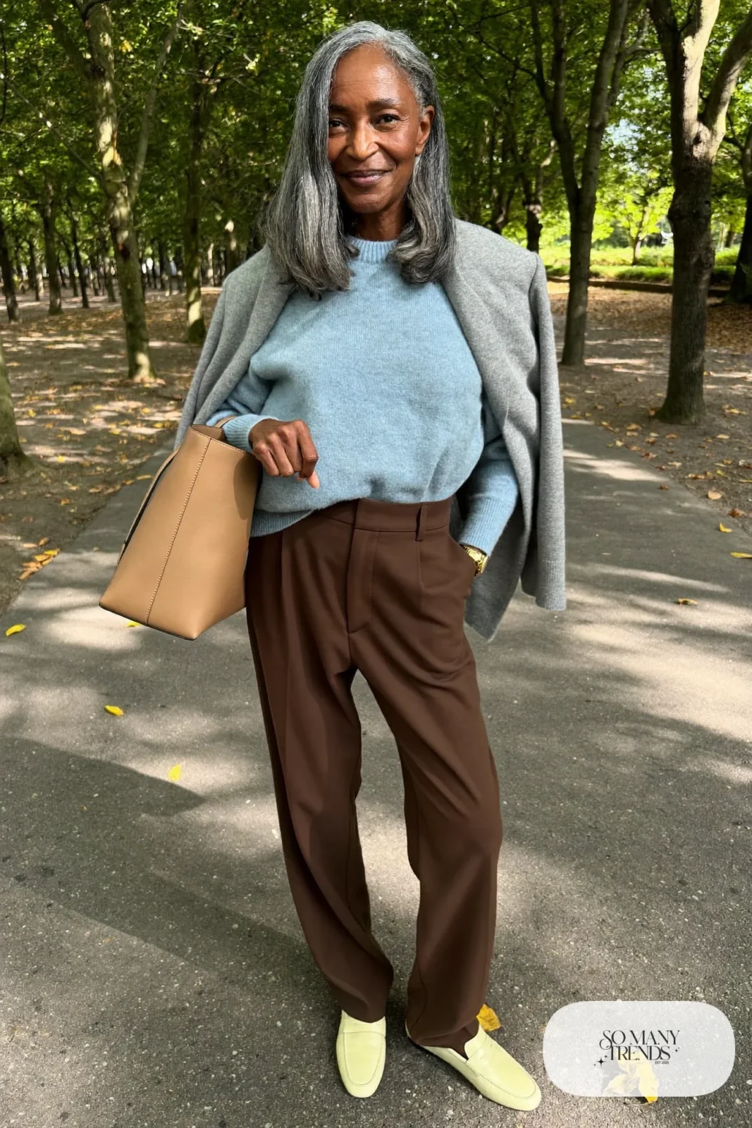 Woman in her sixties wearing a powder blue crewneck sweater, chocolate brown straight pants and cream loafers, outfit 15