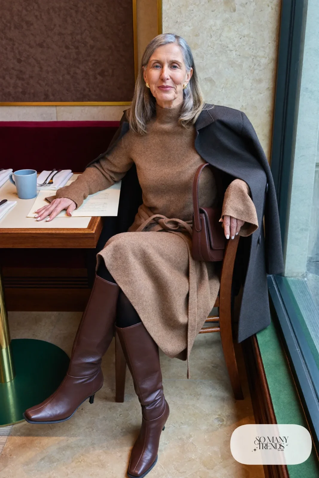 Woman in her sixties wearing a camel knit midi dress with a waist tie, tall brown boots and a chocolate leather bag, outfit 17
