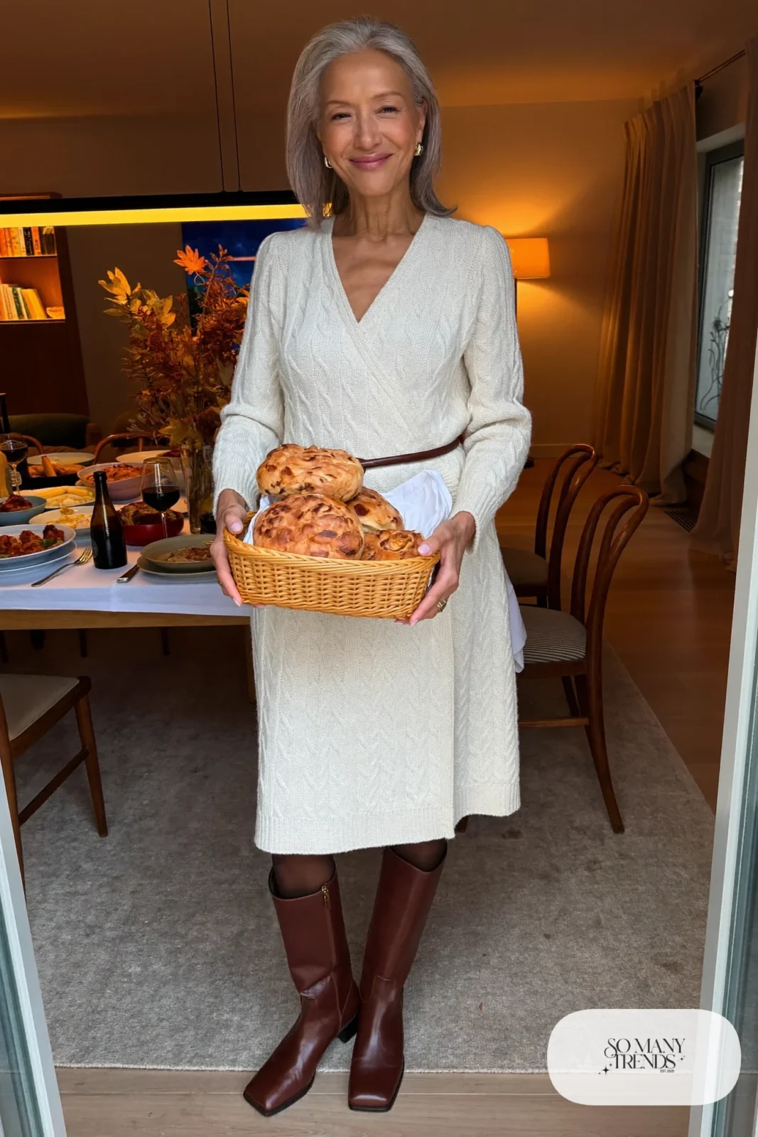 Woman in her sixties wearing a cream cable knit midi sweater dress, a chocolate belt and tall brown boots, outfit 22