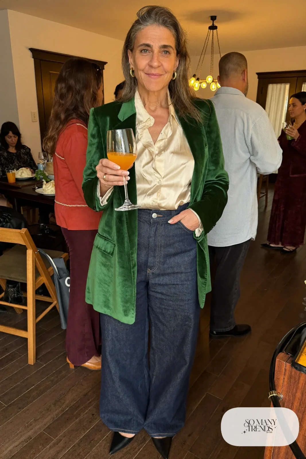 Woman in her sixties wearing a forest green velvet blazer, dark wide-leg jeans, a cream shell and black pointed flats, outfit 28