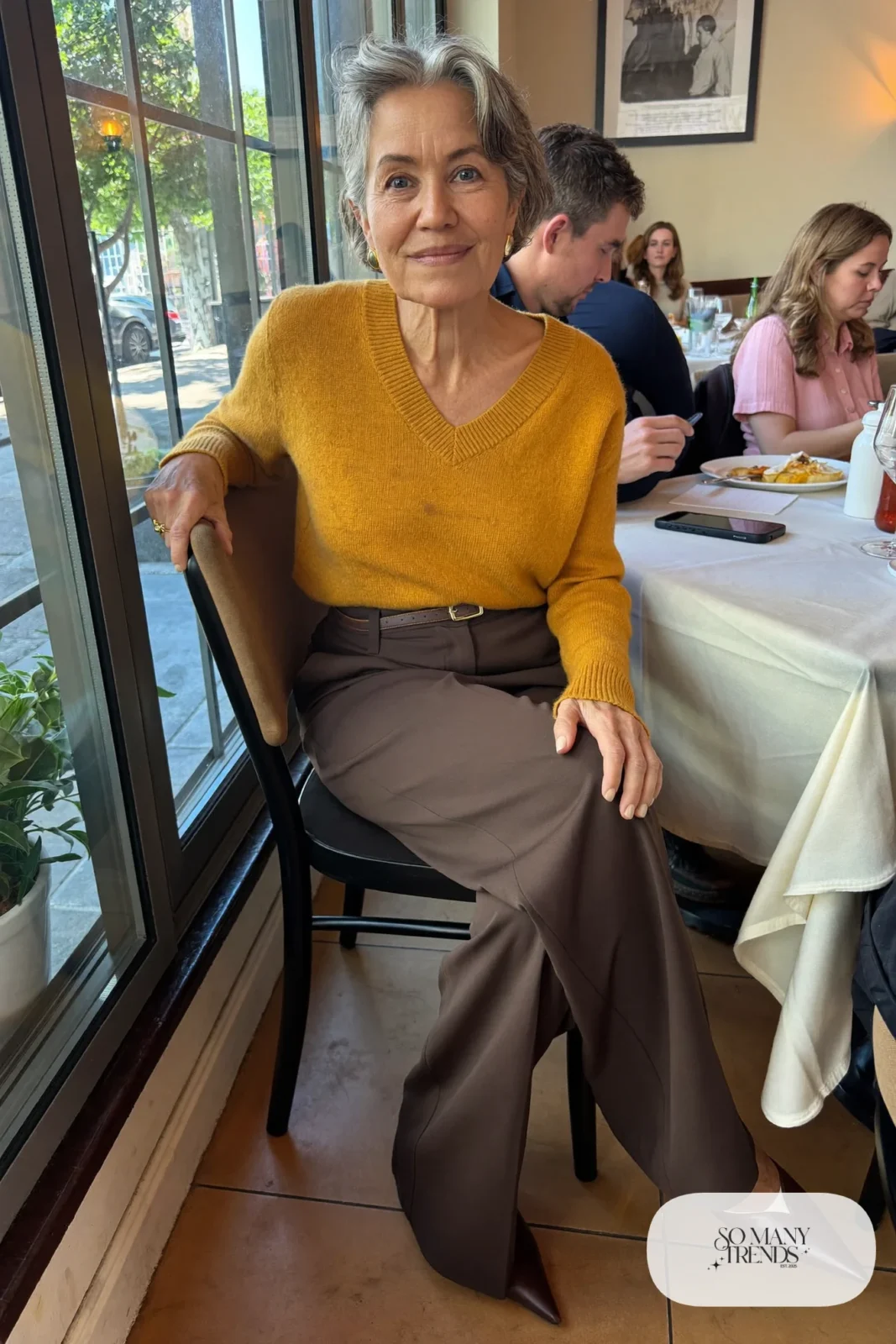 Petite woman in a mustard V-neck sweater tucked into high-waisted chocolate brown wide-leg pants with pointed brown flats, outfit 1