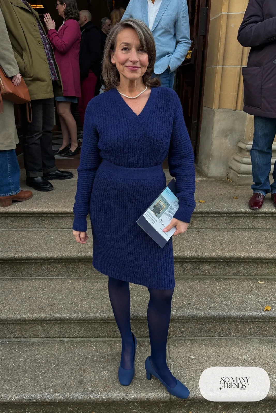 Petite woman in a navy knit V-neck dress below the knee with navy tights and low block heels, outfit 2