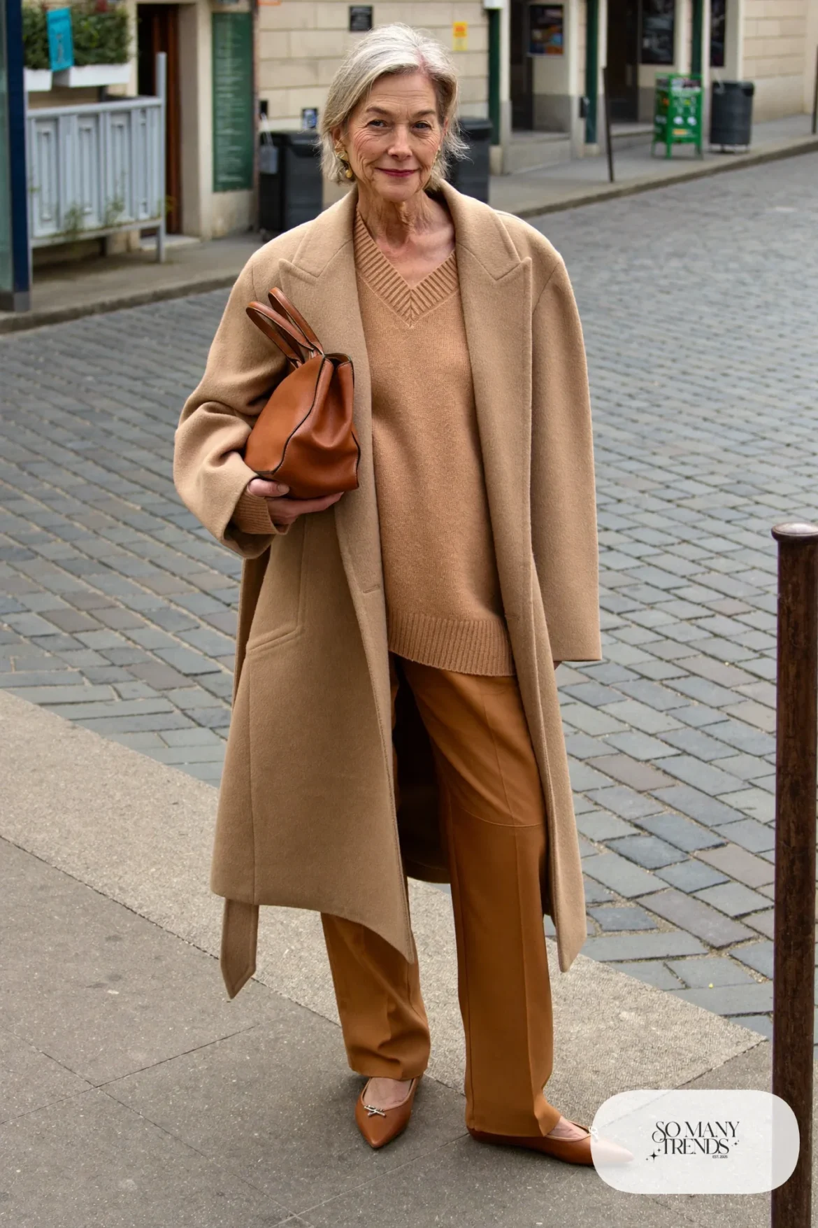 Petite woman in a knee-length camel wool coat open over a tonal camel knit and pants with pointed flats, outfit 13