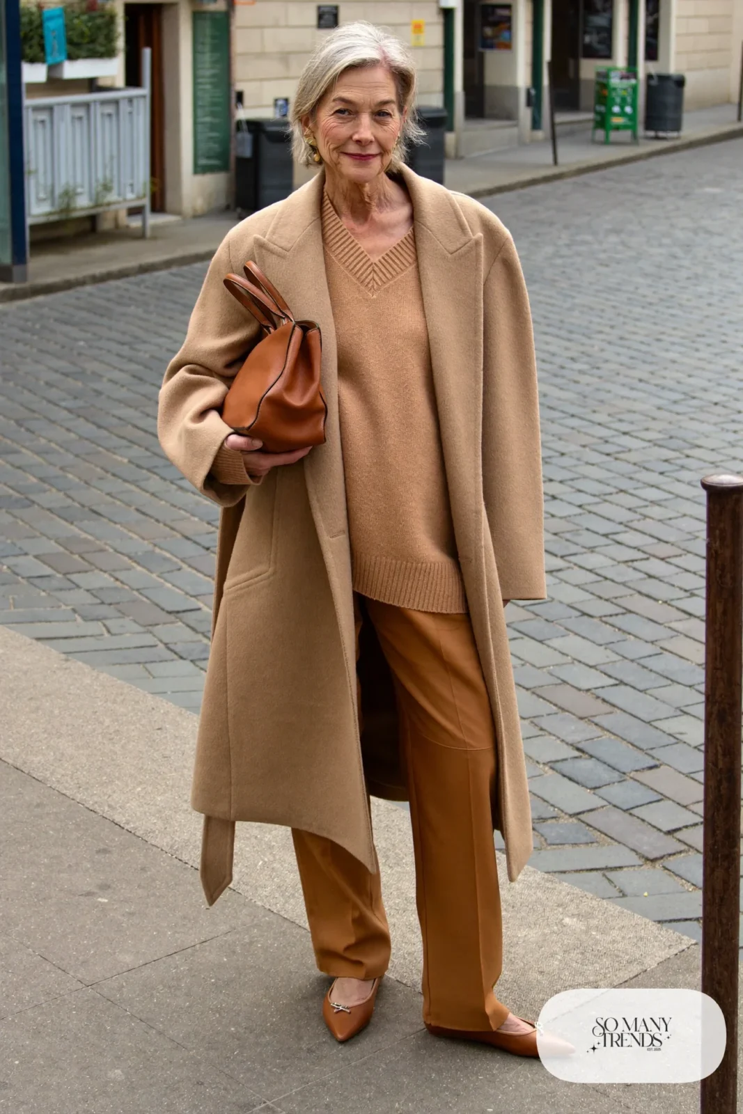 Petite woman in a knee-length camel wool coat open over a tonal camel knit and pants with pointed flats, outfit 13