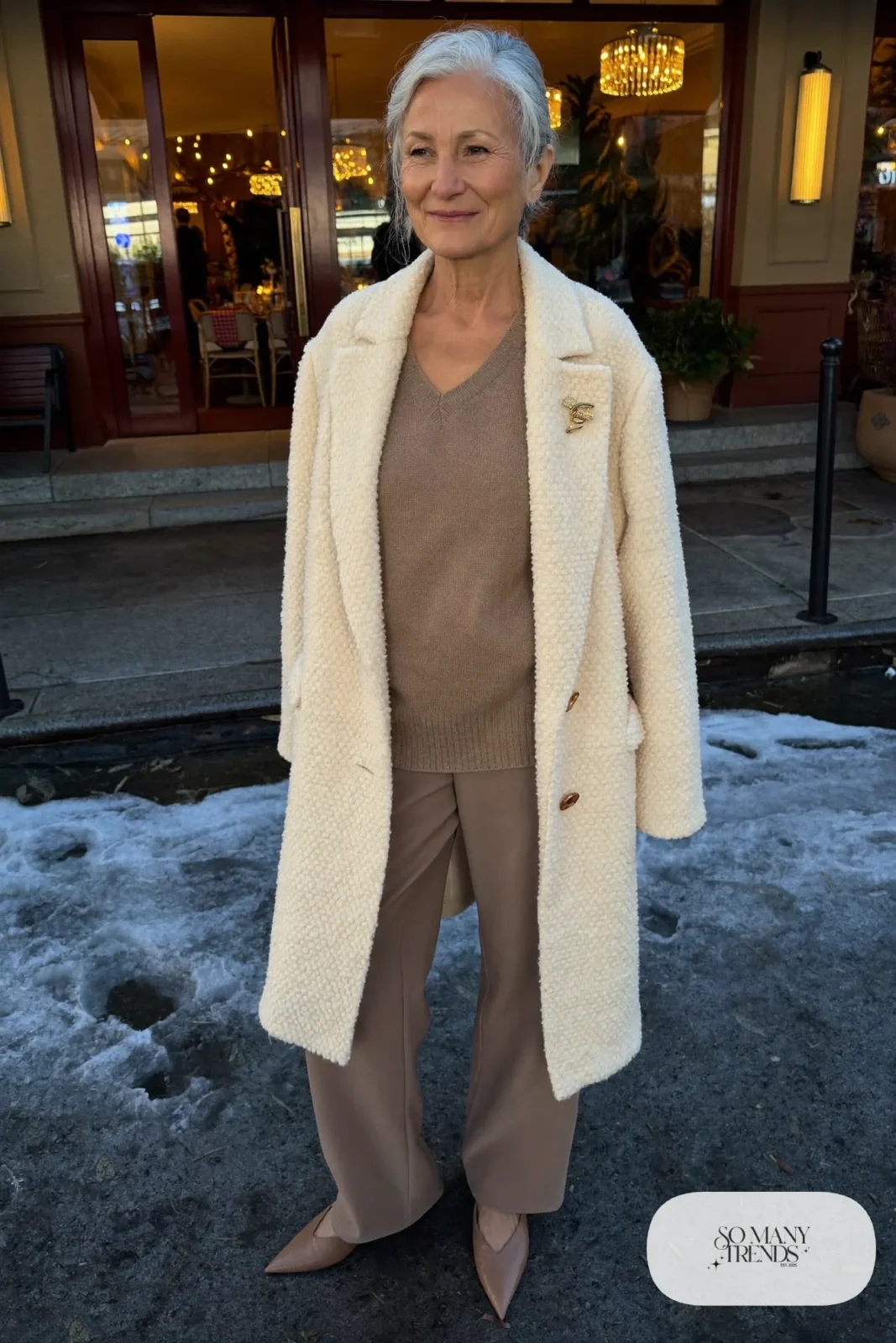 Petite woman in a knee-length cream coat over taupe knit and pants with pointed flats, outfit 16