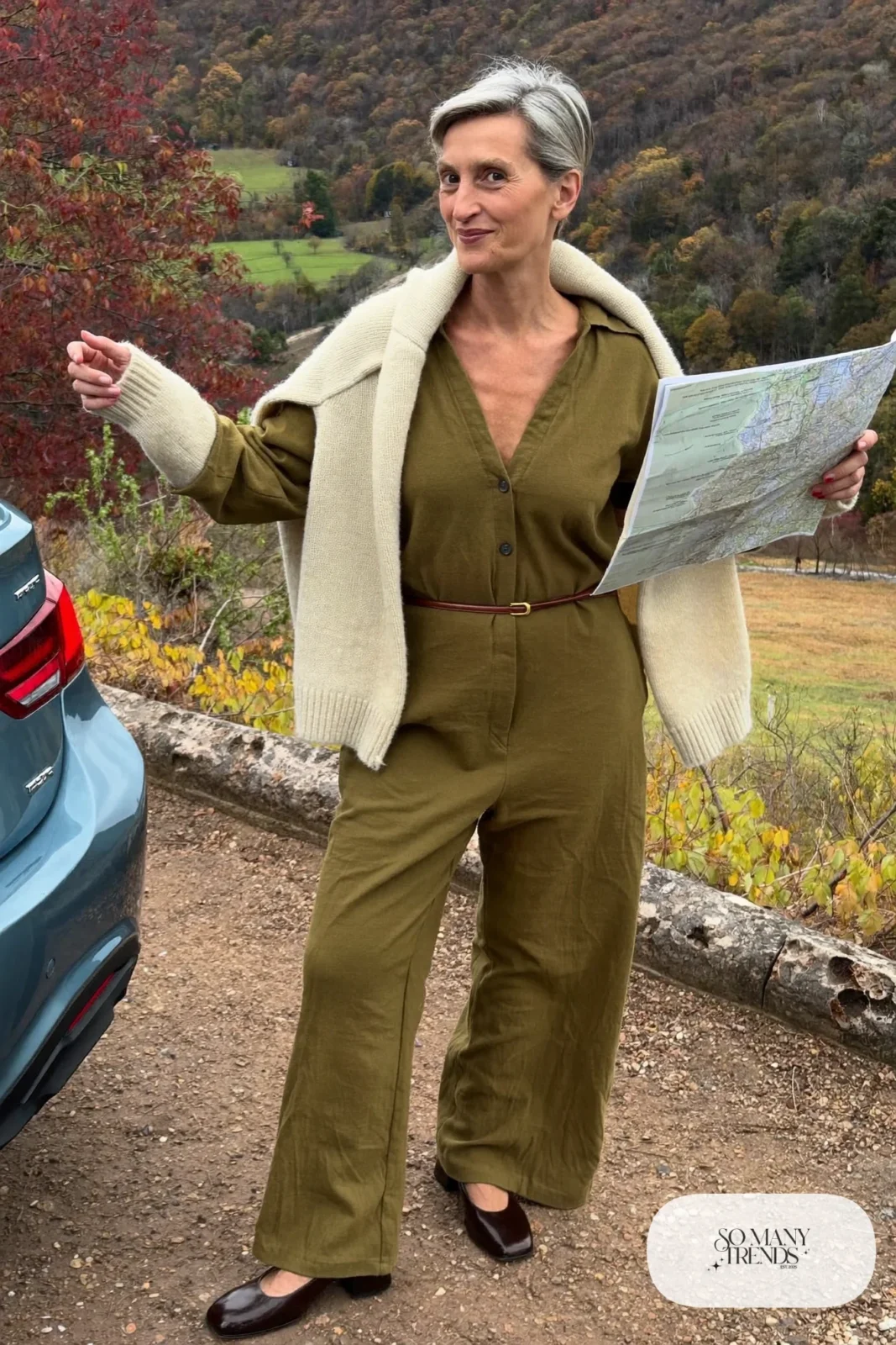Petite woman in an olive wide-leg jumpsuit with a belt and a cream cardigan with low heels while traveling, outfit 22