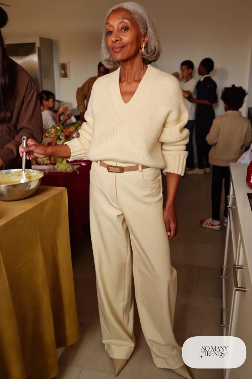 Petite woman in a cream knit top and matching high-waisted wide-leg pants with a thin belt and pointed shoes at a holiday gathering, outfit 26