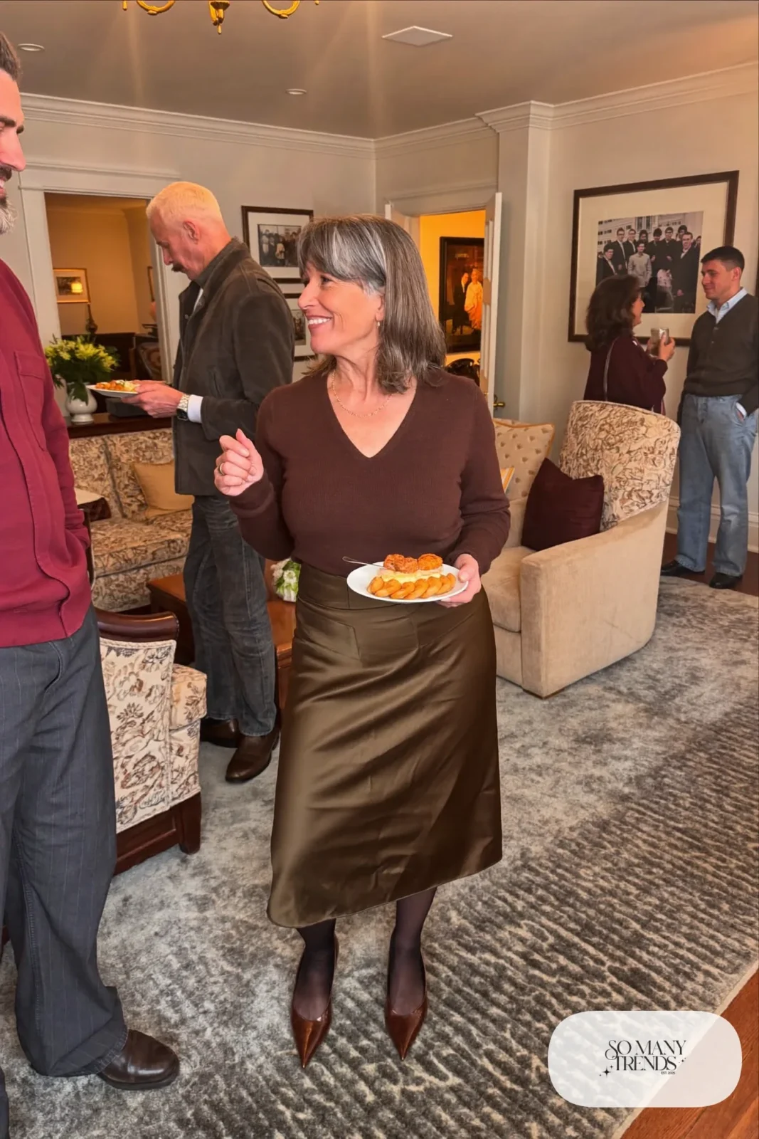 Petite woman in an olive satin midi skirt with a tucked chocolate knit and pointed pumps at a family party, outfit 29