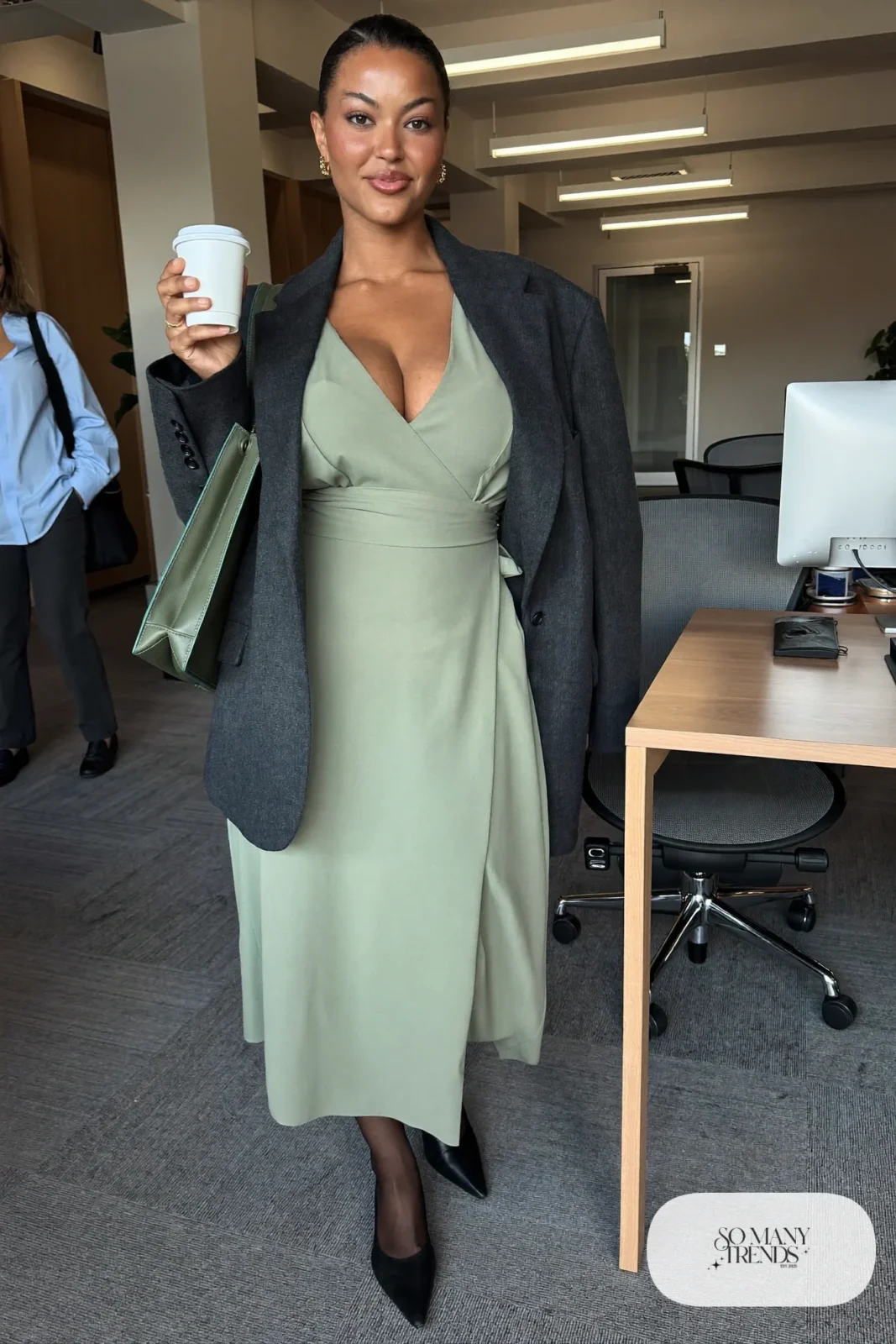Woman in a sage green midi wrap dress with a charcoal blazer and flats, outfit 1