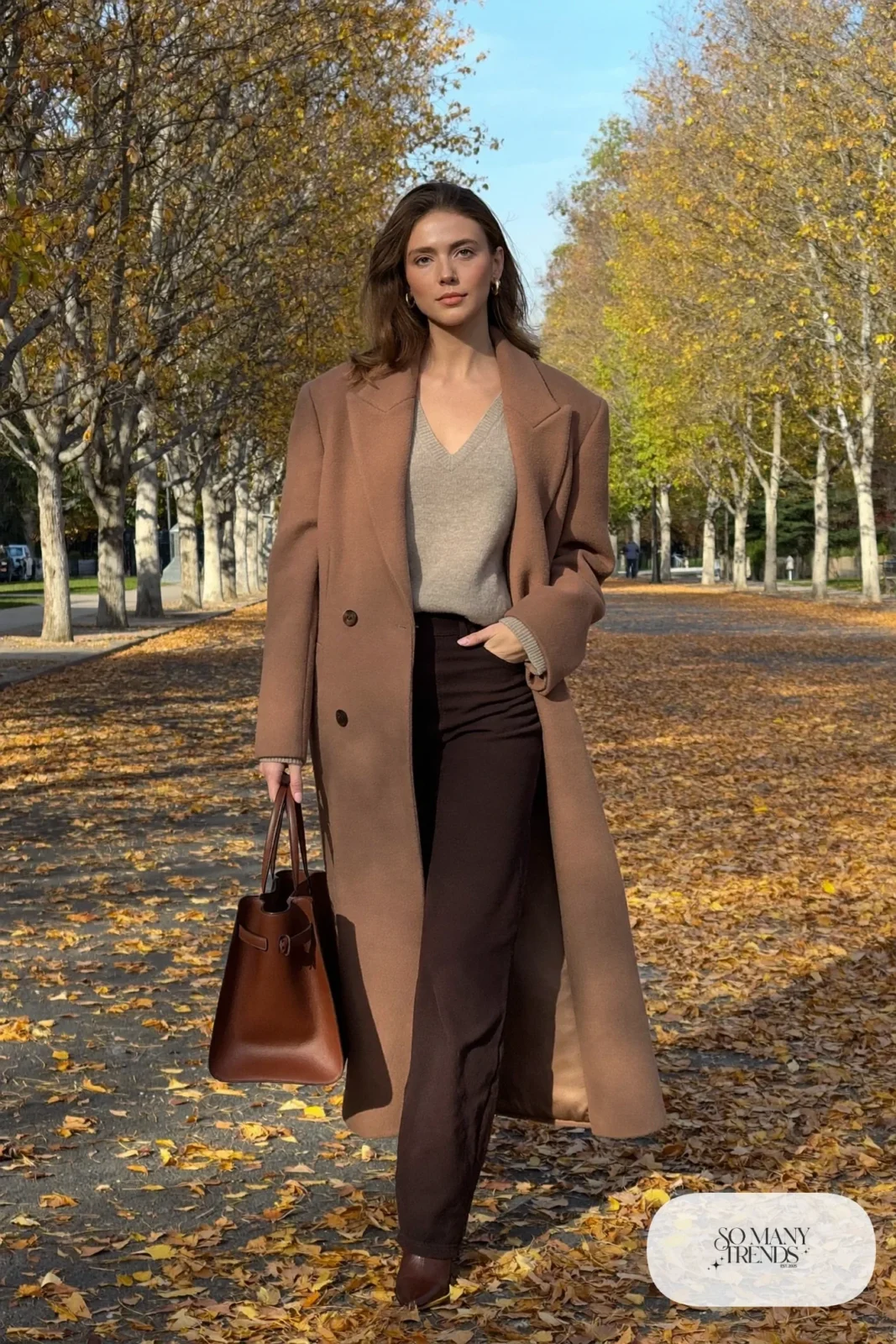Woman in a long camel wool coat over an oatmeal V-neck sweater and espresso pants, outfit 10