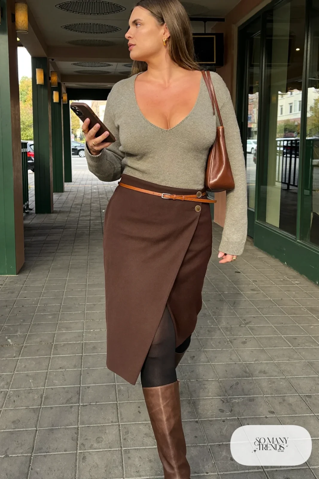 Woman in an espresso wrap midi skirt with a tucked oatmeal V-neck sweater and tall boots, outfit 19
