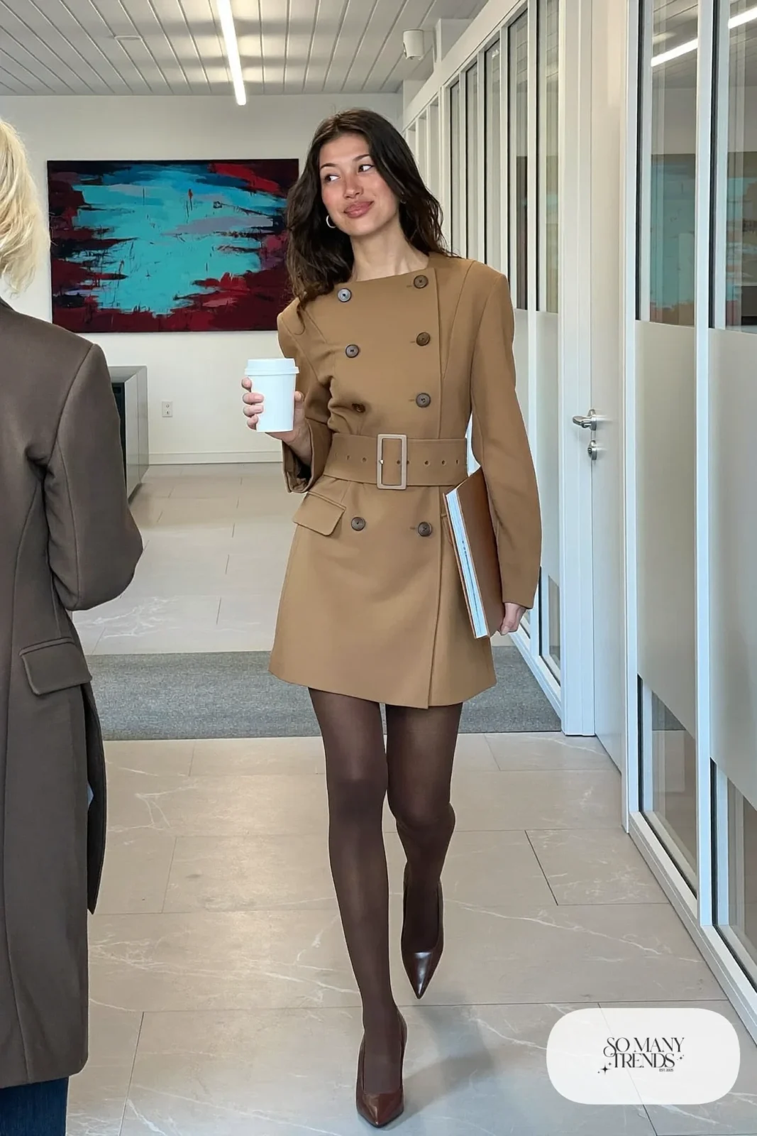 Woman with a straight athletic figure in a camel belted blazer dress with opaque tights and pointed pumps in an office hallway, outfit 13