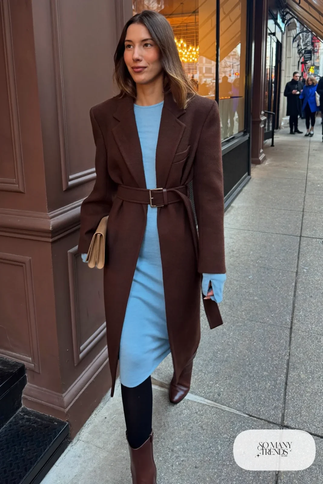 Woman with a straight athletic figure in a baby blue knit top and skirt under a long belted chocolate coat with boots, outfit 29