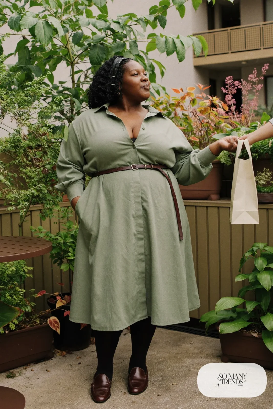 Woman in sage cotton shirt dress with a brown belt, black tights and brown loafers, outfit 11